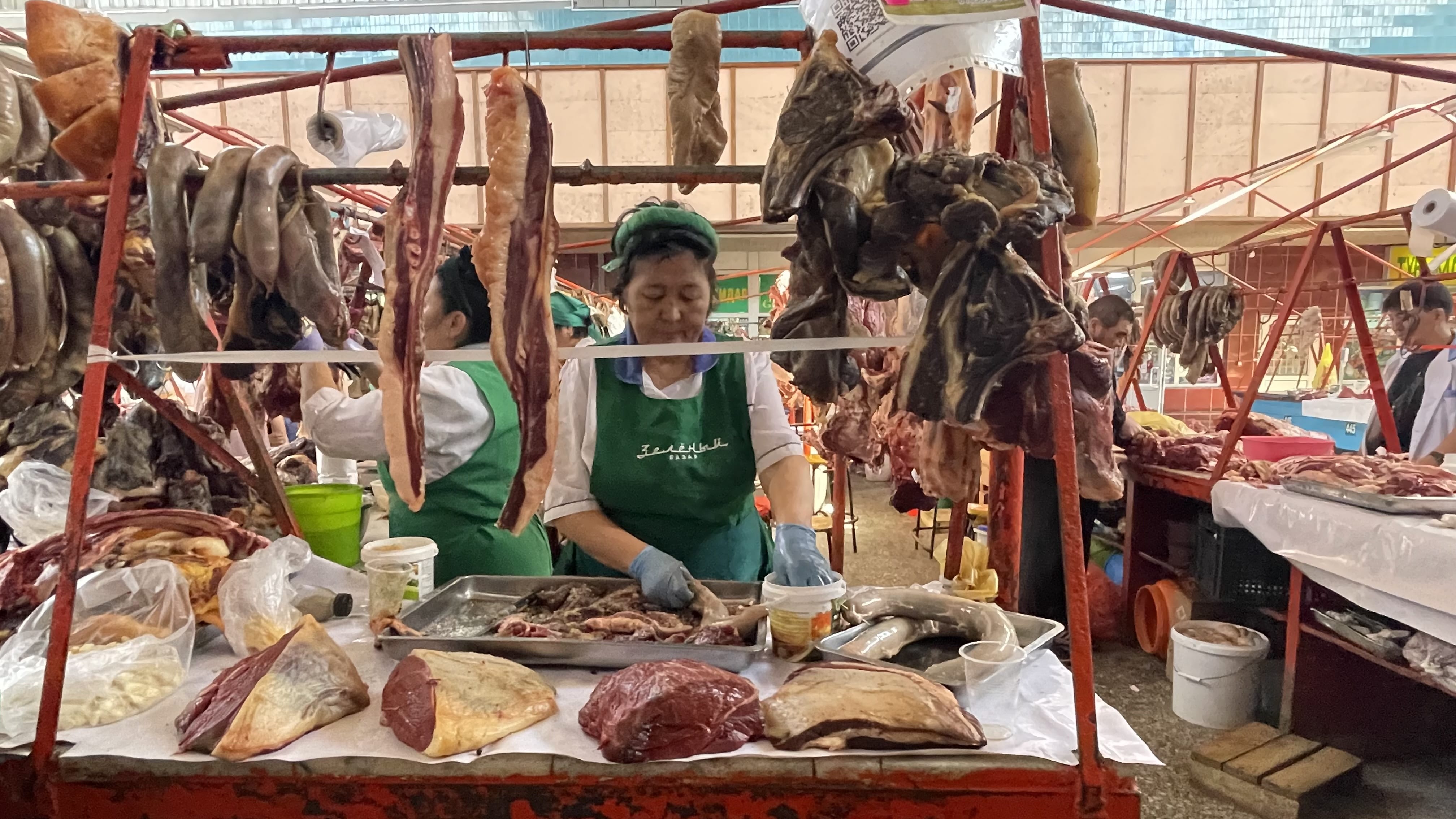 Meat vendors at the Green Market in Almaty selling cuts of horse meat and sausages, including kazy, at a traditional market stall