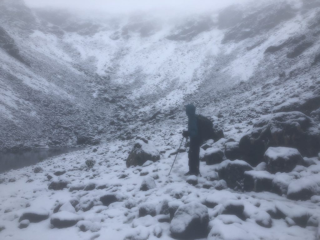 Trekker navigating a snow-covered rocky basin on Mount Kenya in heavy fog.
