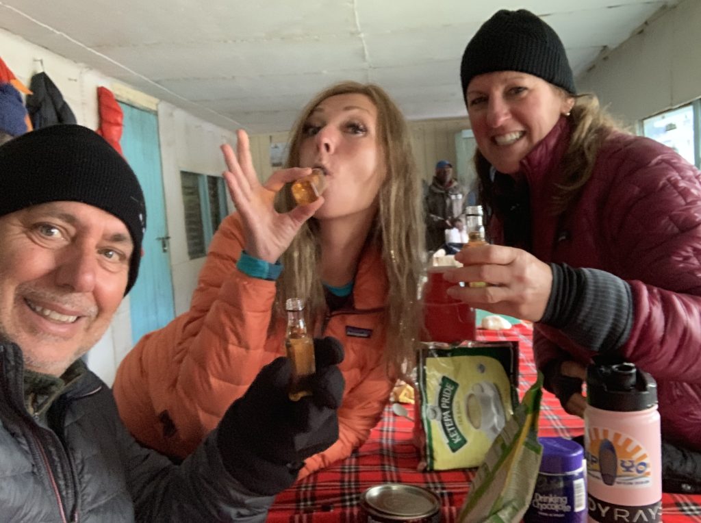 Hikers celebrating inside a hut after Mount Kenya summit day with drinks and warm layers.