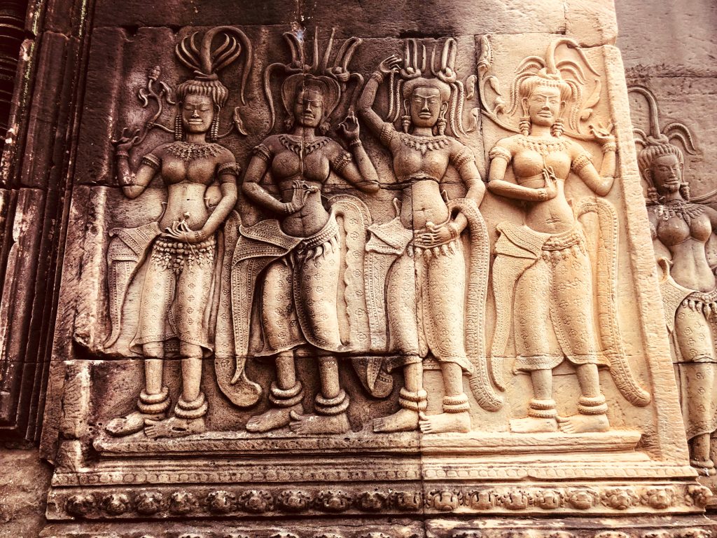 Intricate stone carvings of Apsara dancers on a temple wall at Angkor Wat in Siem Reap, Cambodia, showing detailed costumes, headdresses, and hand gestures.