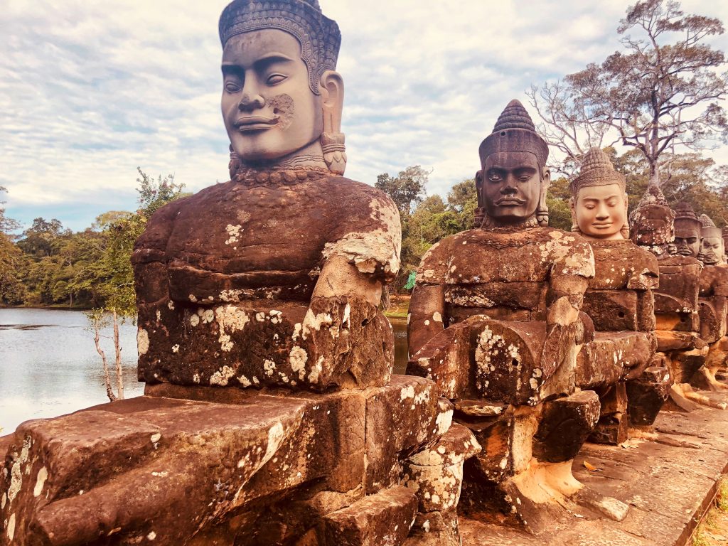 Row of stone statues depicting gods (devas) holding a naga serpent along the causeway leading to the South Gate of Angkor Thom in Siem Reap, Cambodia.