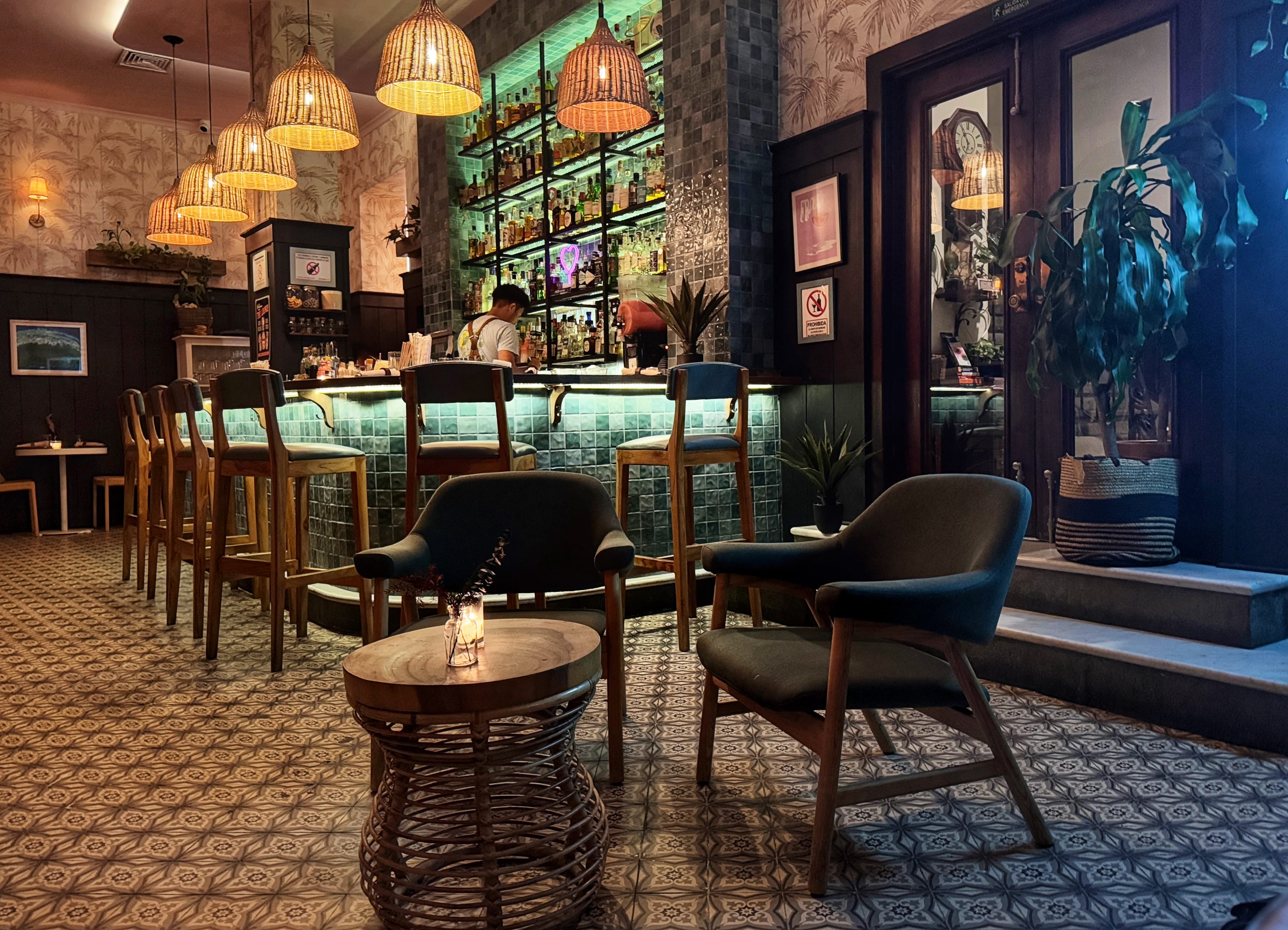 Cozy interior of Mahalo Cocina y Jardín in Panama City, with wicker lamps, a glowing bar, and stylish modern furniture.