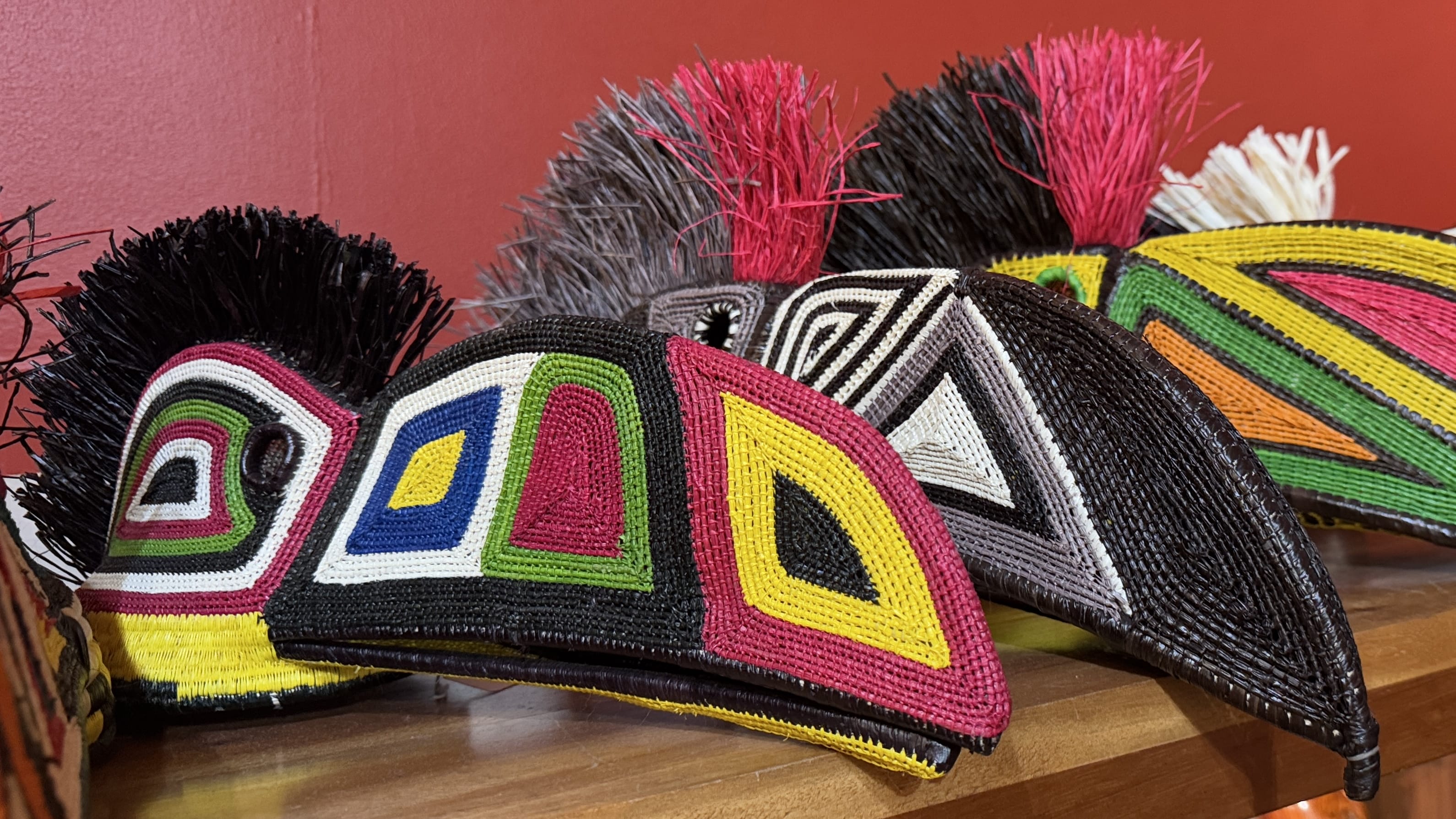 Close-up of traditional Panamanian woven masks with bold geometric patterns in red, yellow, green, and black, displayed against a red wall.