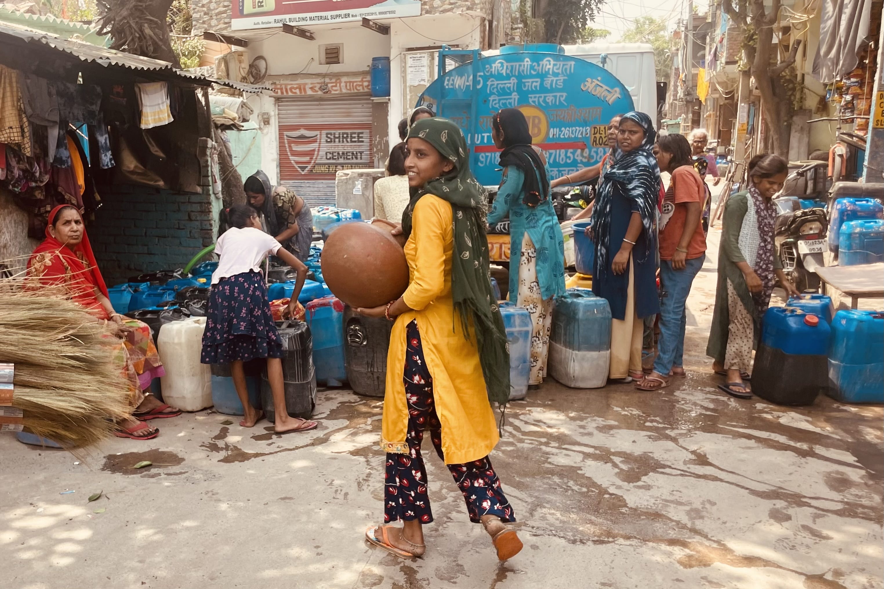 Women and children gather around jerry cans and a water truck in a residential Delhi neighborhood.
