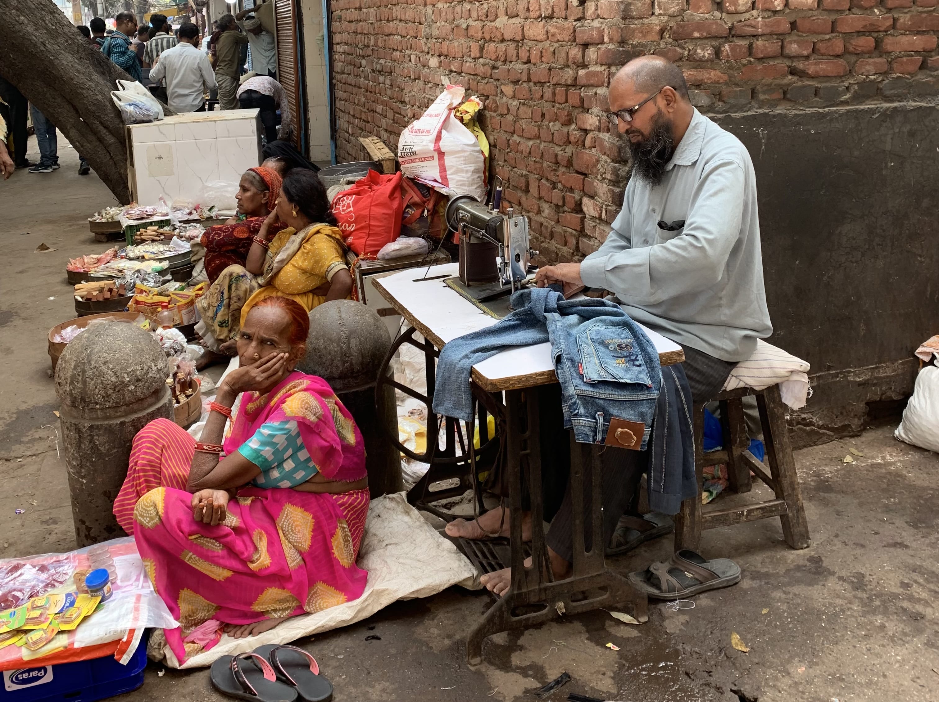 Sidewalk tailor sewing jeans in an alley in Old Delhi