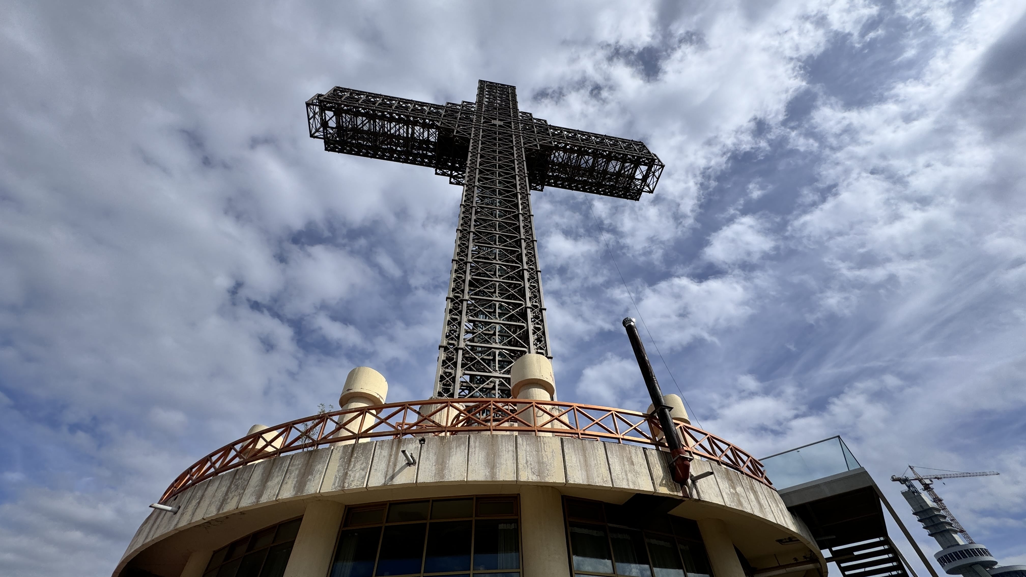 A dramatic upward view of the Millennium Cross on Mount Vodno, North Macedonia, set against a cloudy sky.
