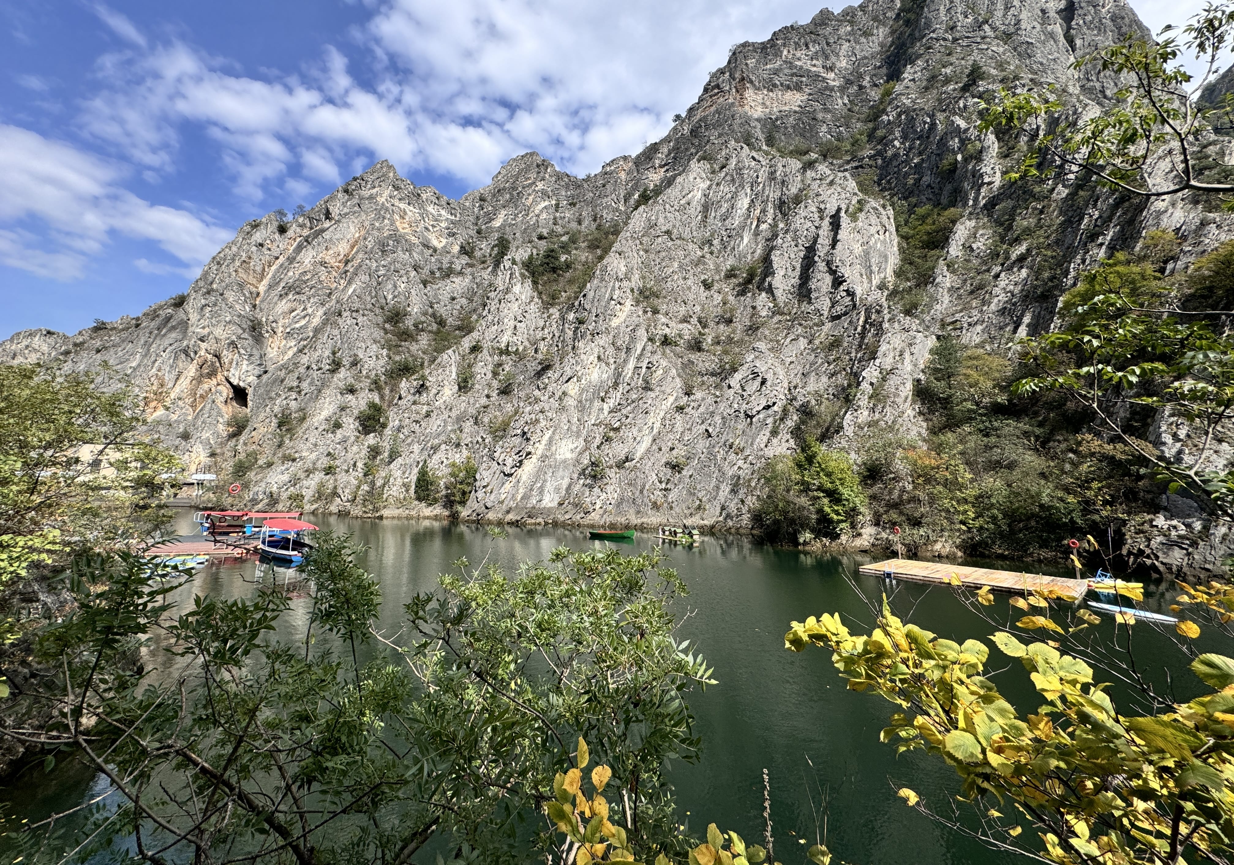 Steep rocky cliffs rising above the emerald waters of Matka Canyon, with small boats docked along the shore.