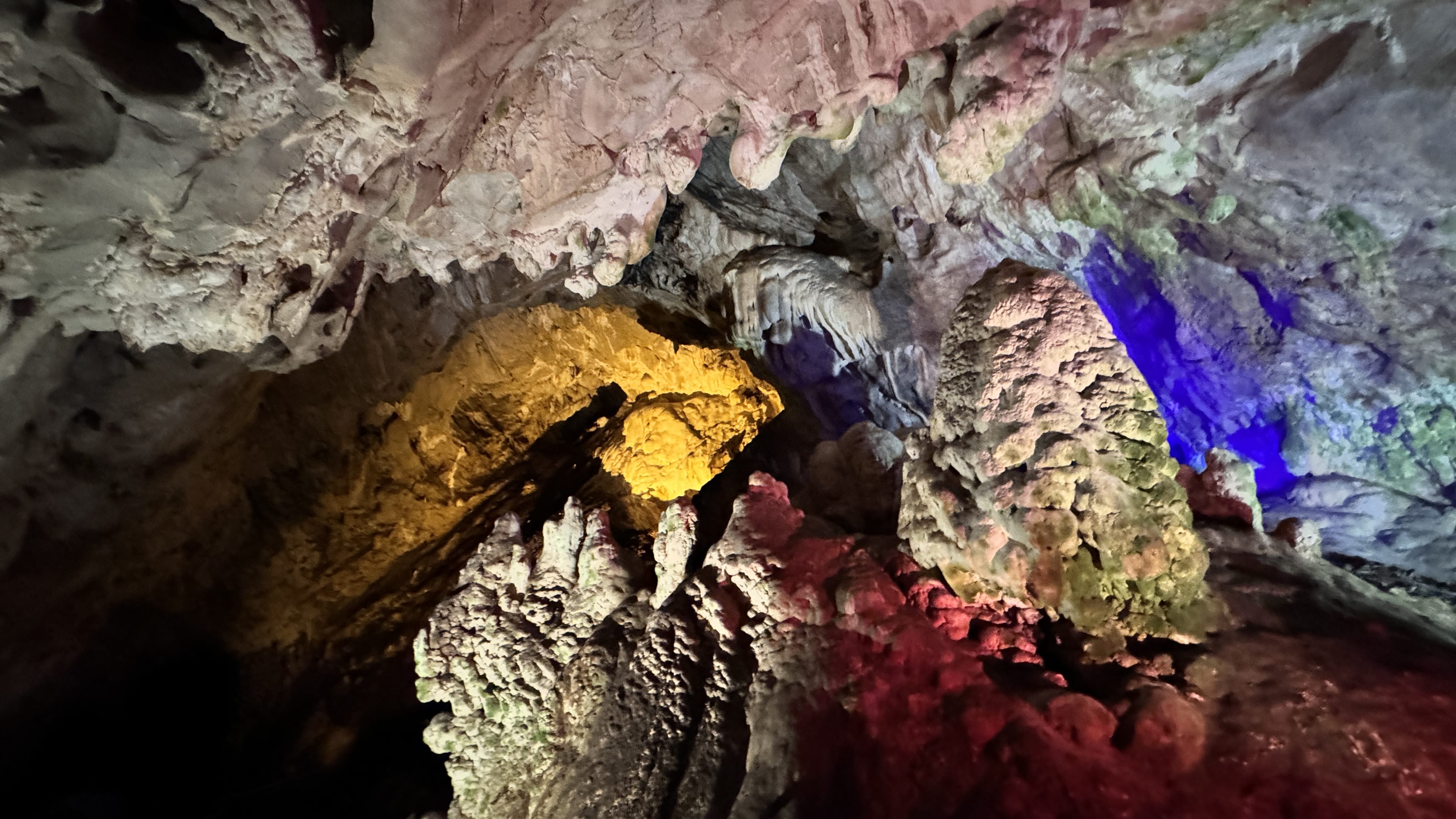 Illuminated cave interior with rock formations glowing in red, yellow, purple, and blue light.