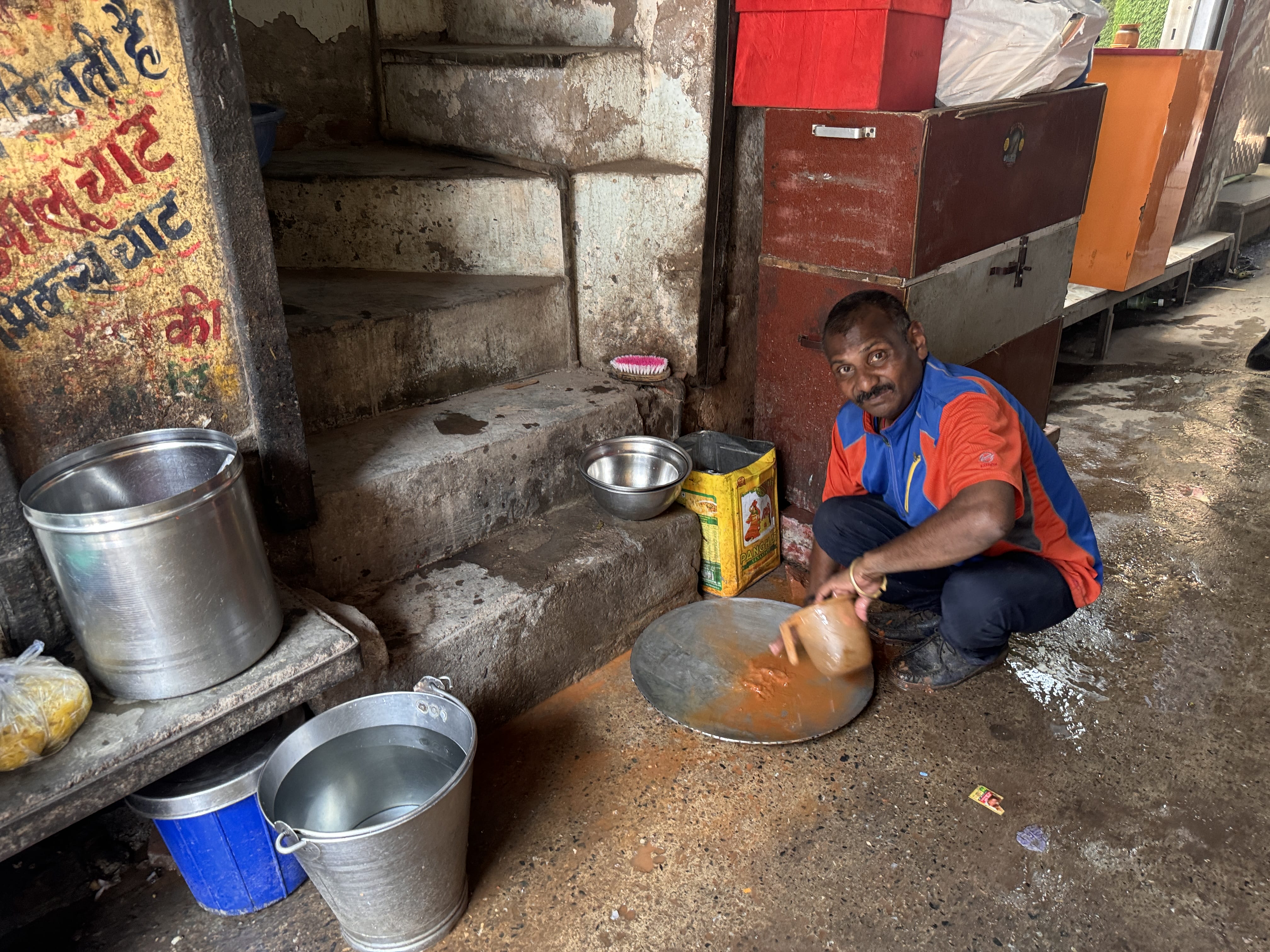 Worker washing a large metal tray behind market stalls in Old Delhi