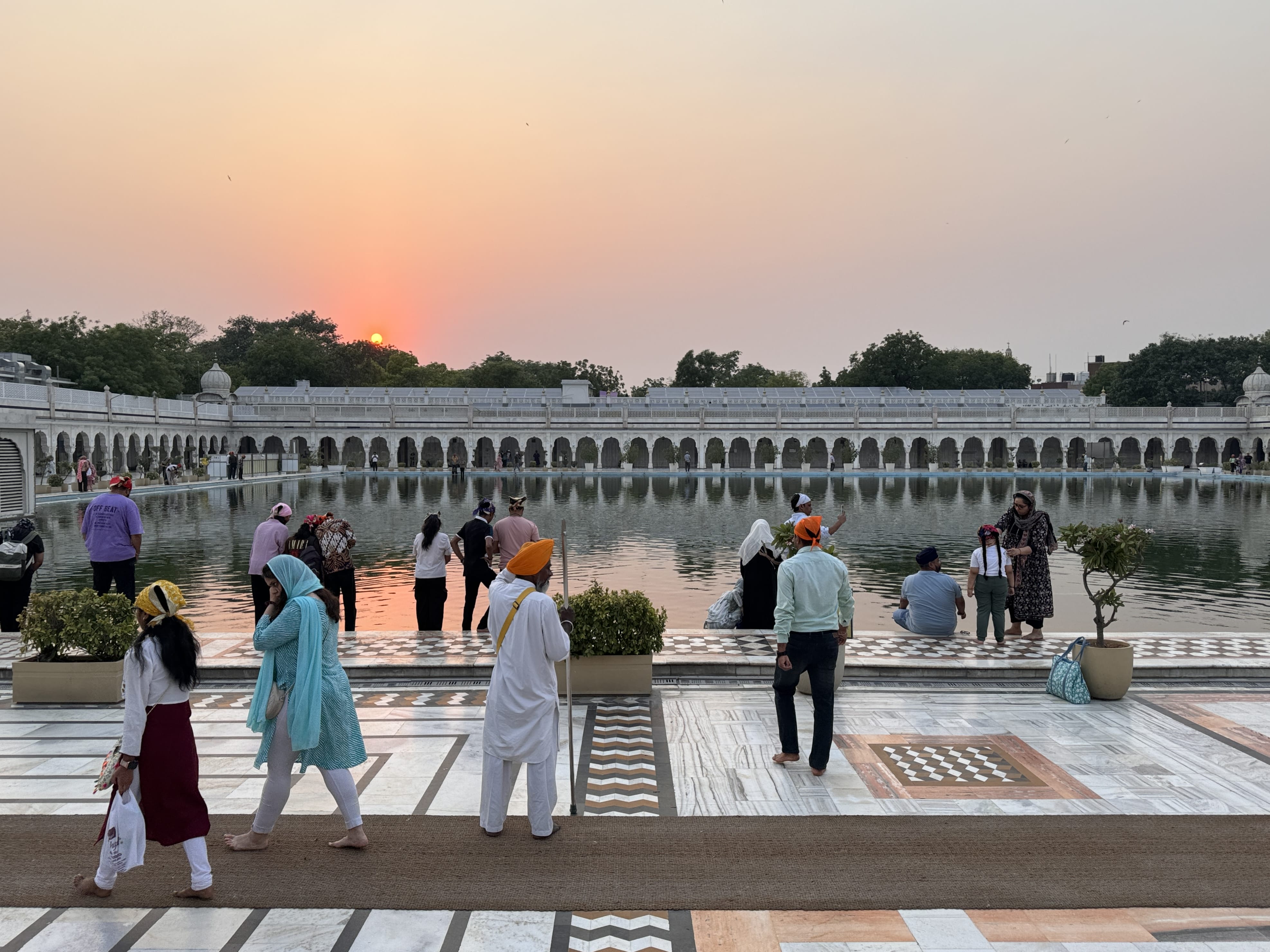 Visitors walking and sitting near the sacred pond of Gurudwara Bangla Sahib at sunset.