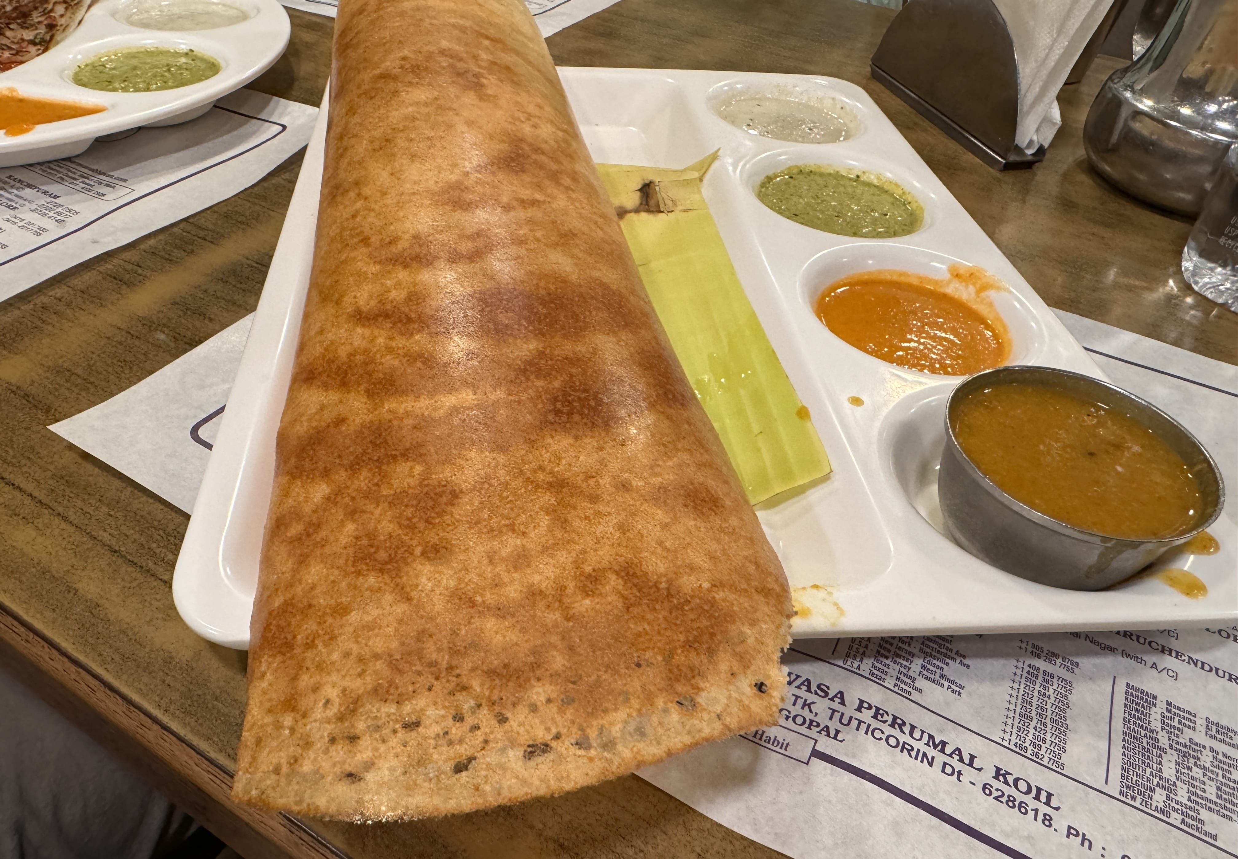 Crispy masala dosa served with sambar and three types of chutney on a tray at a South Indian restaurant in Delhi.