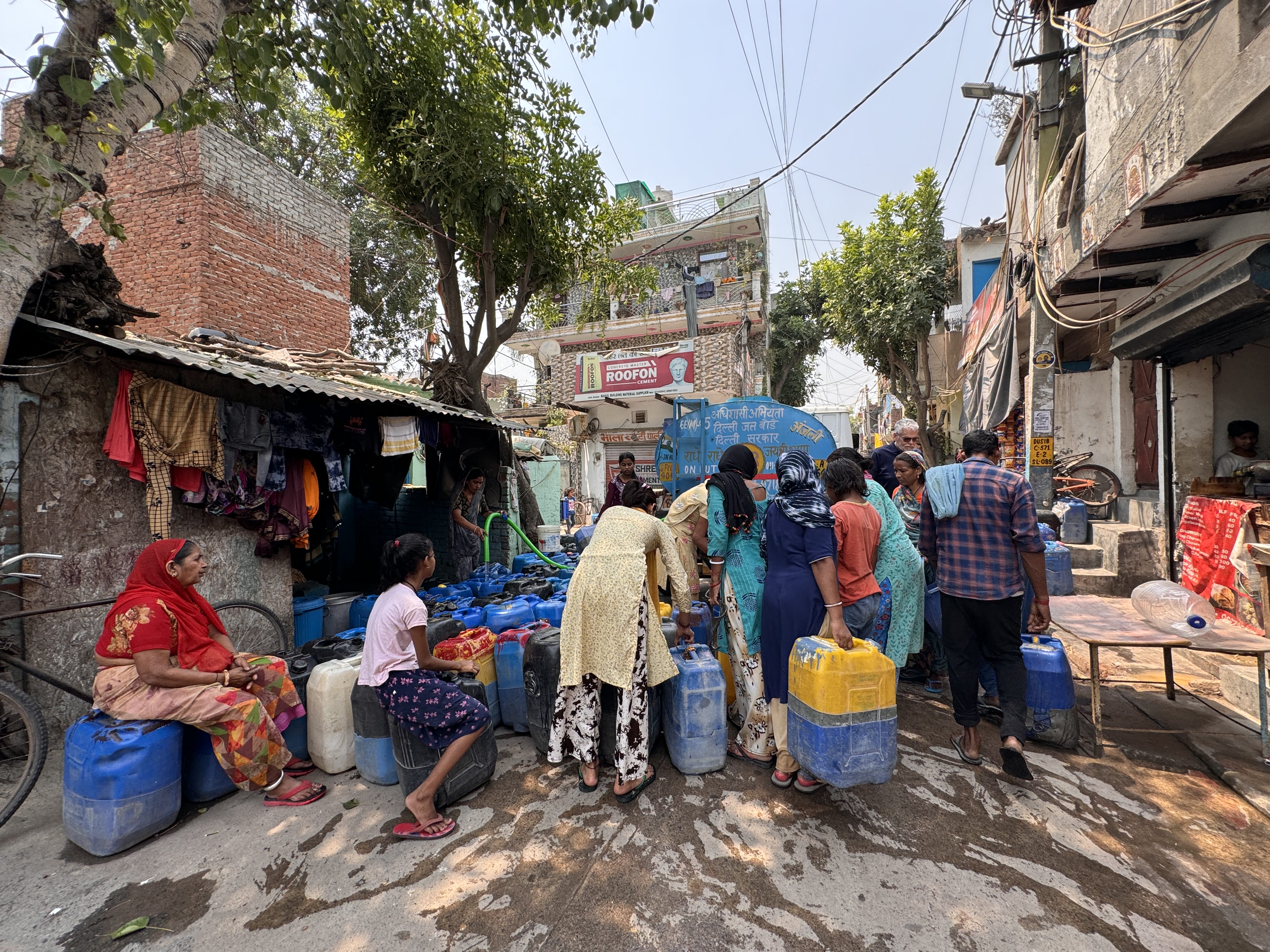 Residents in a Delhi neighborhood gather around large blue containers as a government water truck makes its delivery.