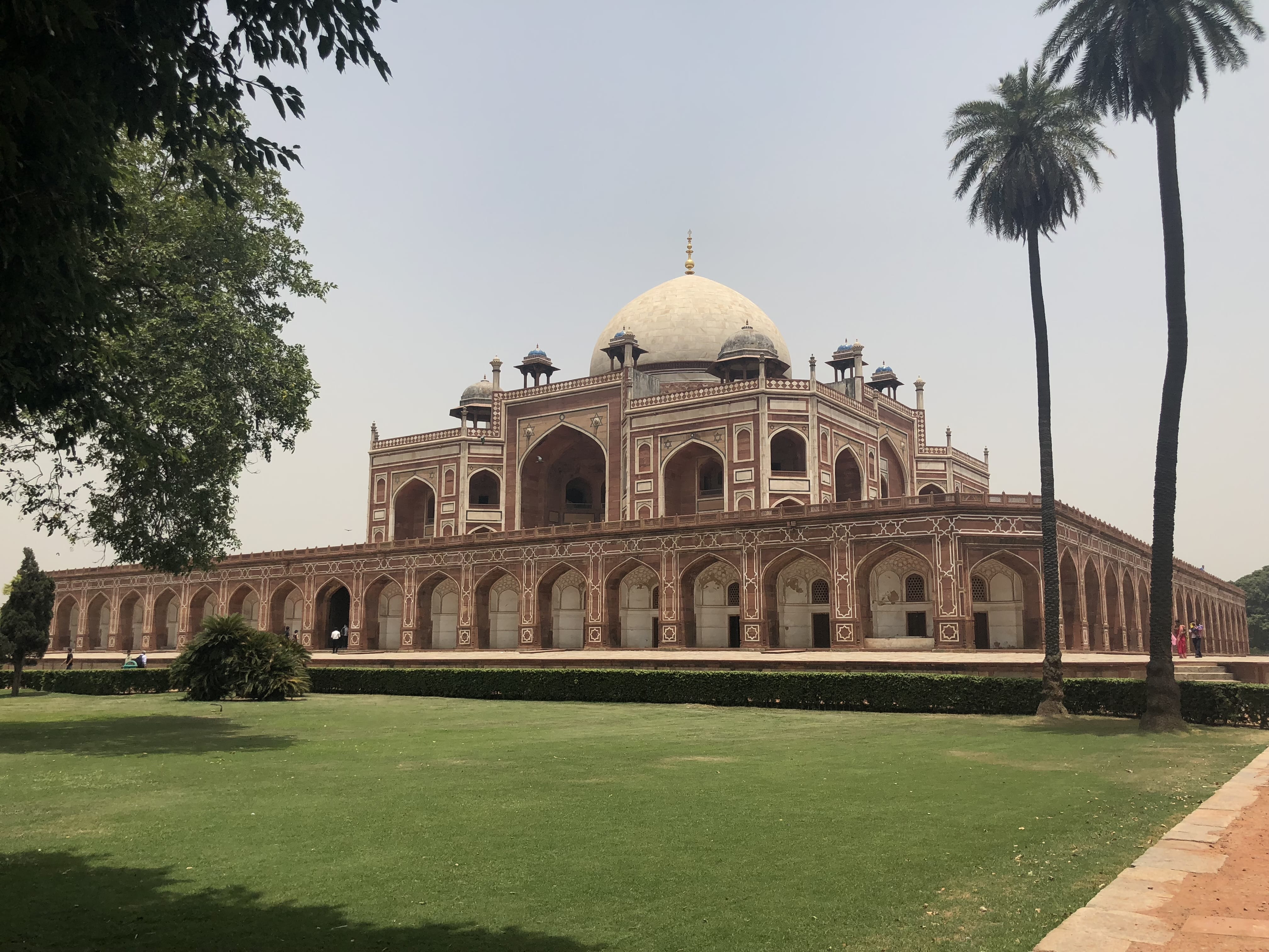 Humayun’s Tomb in Delhi, a grand red sandstone and white marble structure with a central dome, surrounded by palm trees and a manicured lawn.