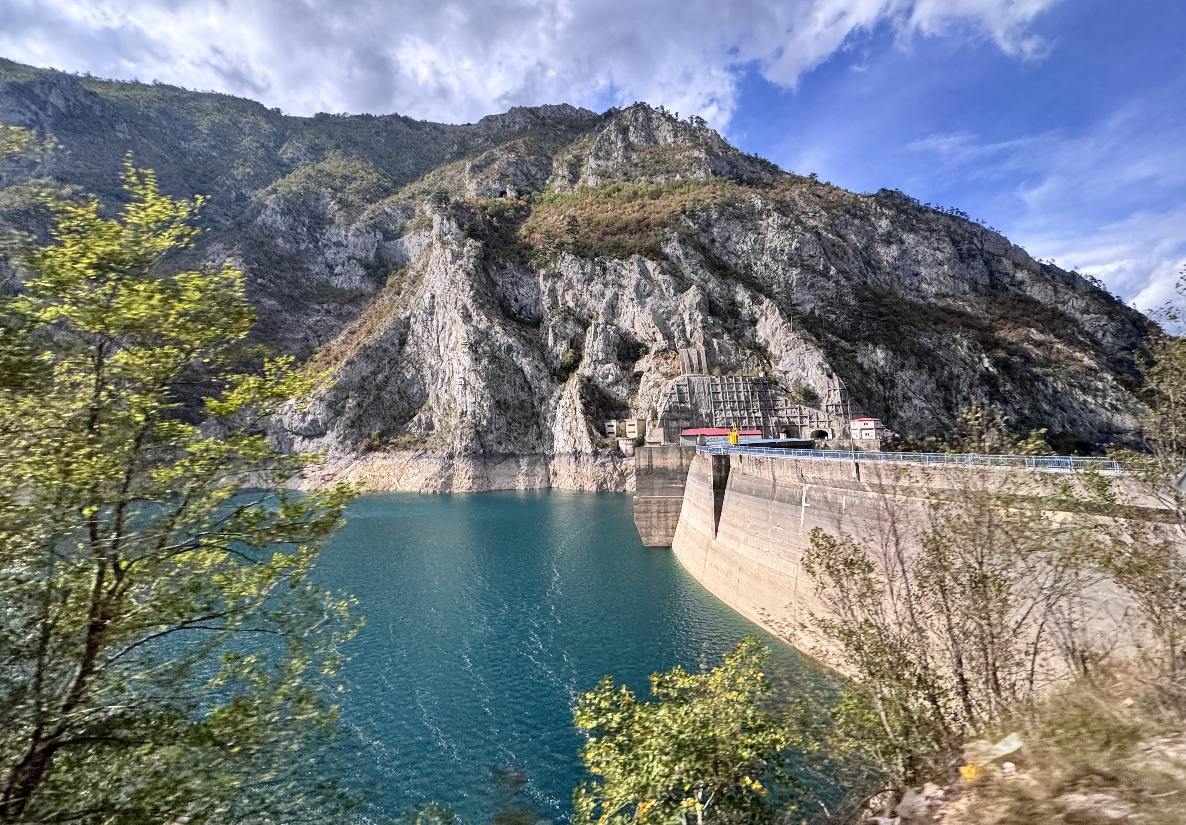 Concrete dam with a road running across it, set against turquoise water and steep rocky cliffs in Bosnia and Herzegovina.