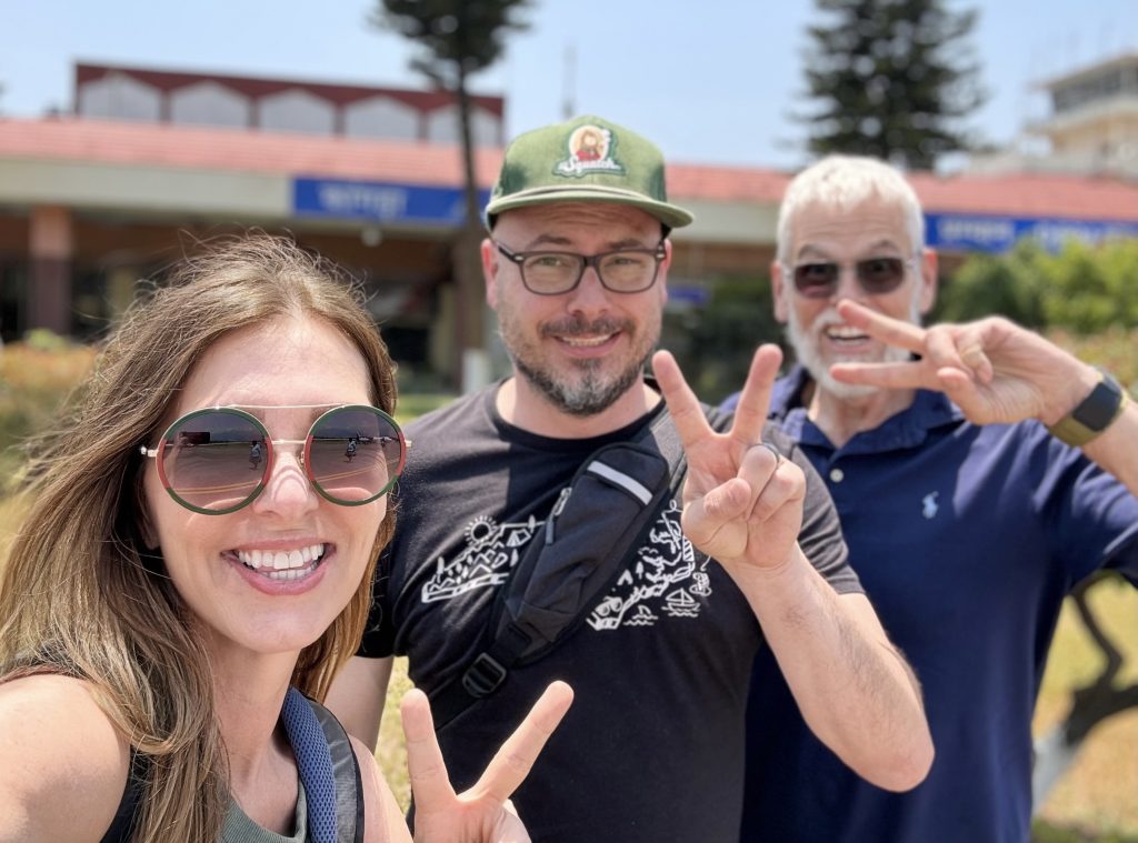 Woman, adult son, and older man smiling and flashing peace signs in front of Kangra Airport- McLeod Ganj itinerary