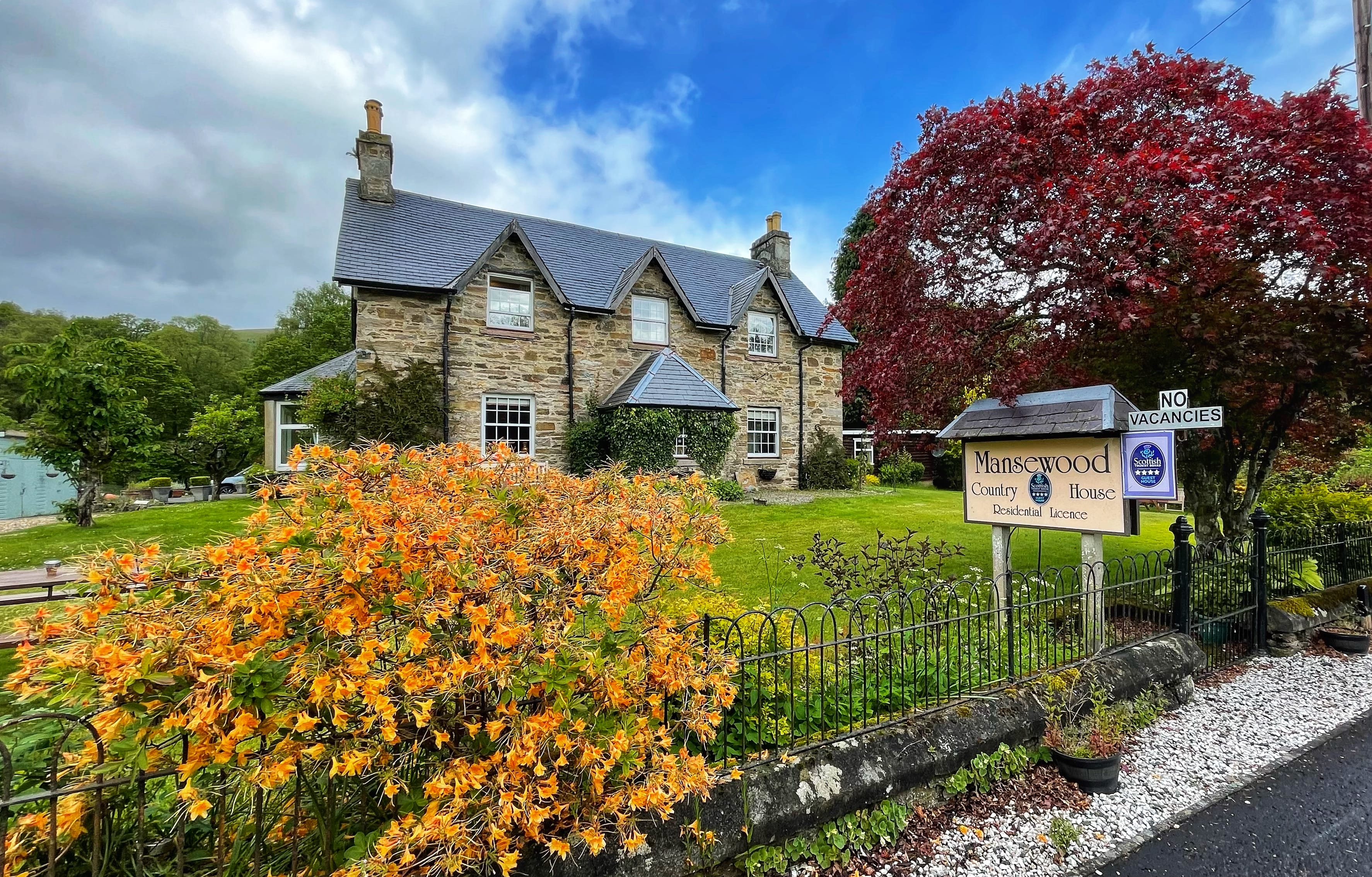 stone country house framed by bright orange and red flowers, with a sign reading “Mansewood Country House.