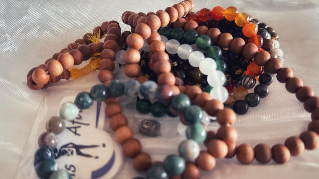 A collection of Tibetan prayer beads made from wood, gemstone, and crystal, laid out on a cloth before being blessed.