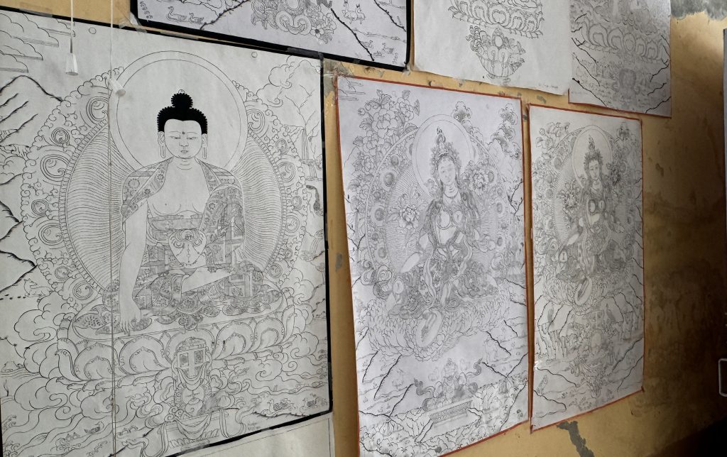 Black-and-white sketches of Buddha and other deities pinned to a workshop wall, rich in fine detail.