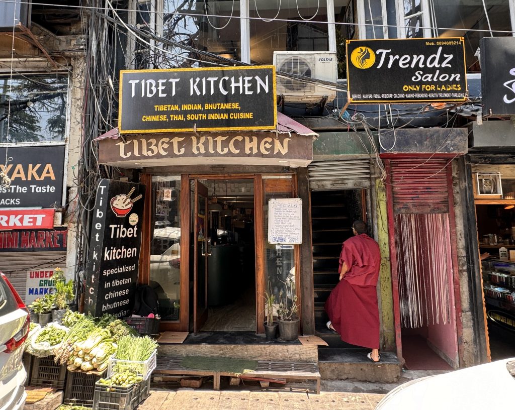 A monk in red robes climbs the stairs beside the entrance to Tibet Kitchen, a restaurant in McLeod Ganj offering Tibetan, Indian, Bhutanese, Chinese, Thai, and South Indian cuisine- McLeod Ganj itinerary