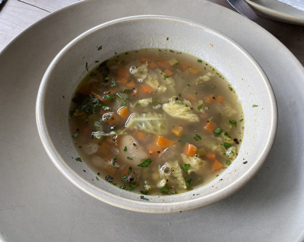 Bowl of vegetable soup with carrots, cabbage, and herbs served on a neutral-toned plate.
