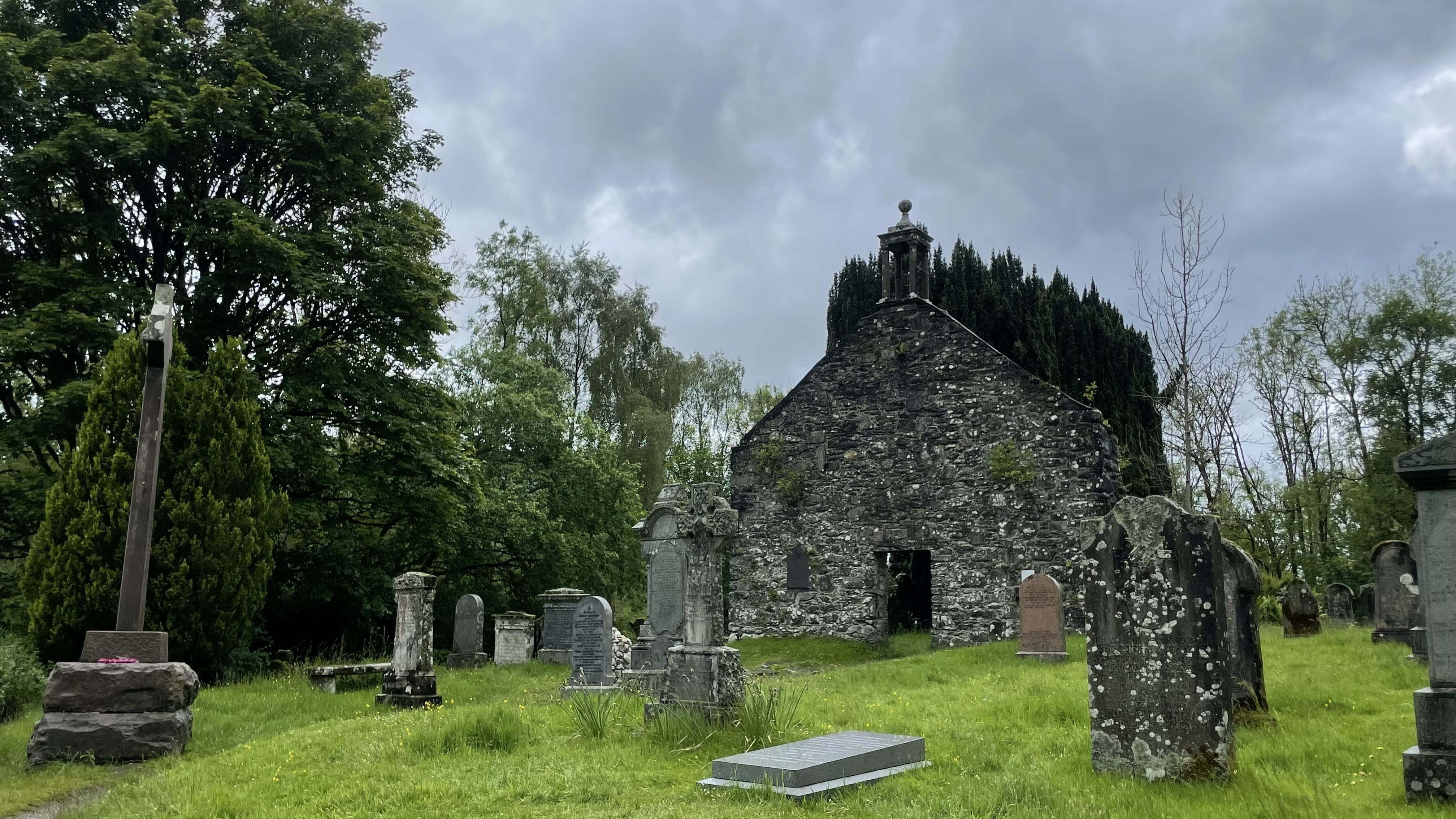 Stone church and cemetery under a cloudy sky, with trees and green hills surrounding the grounds-detour while hiking the Roy Roy Way, Scotland