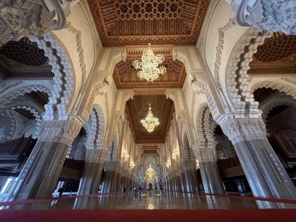 Ornate interior of Hassan II Mosque in Casablanca, showing carved arches, chandeliers, and detailed wooden ceilings.