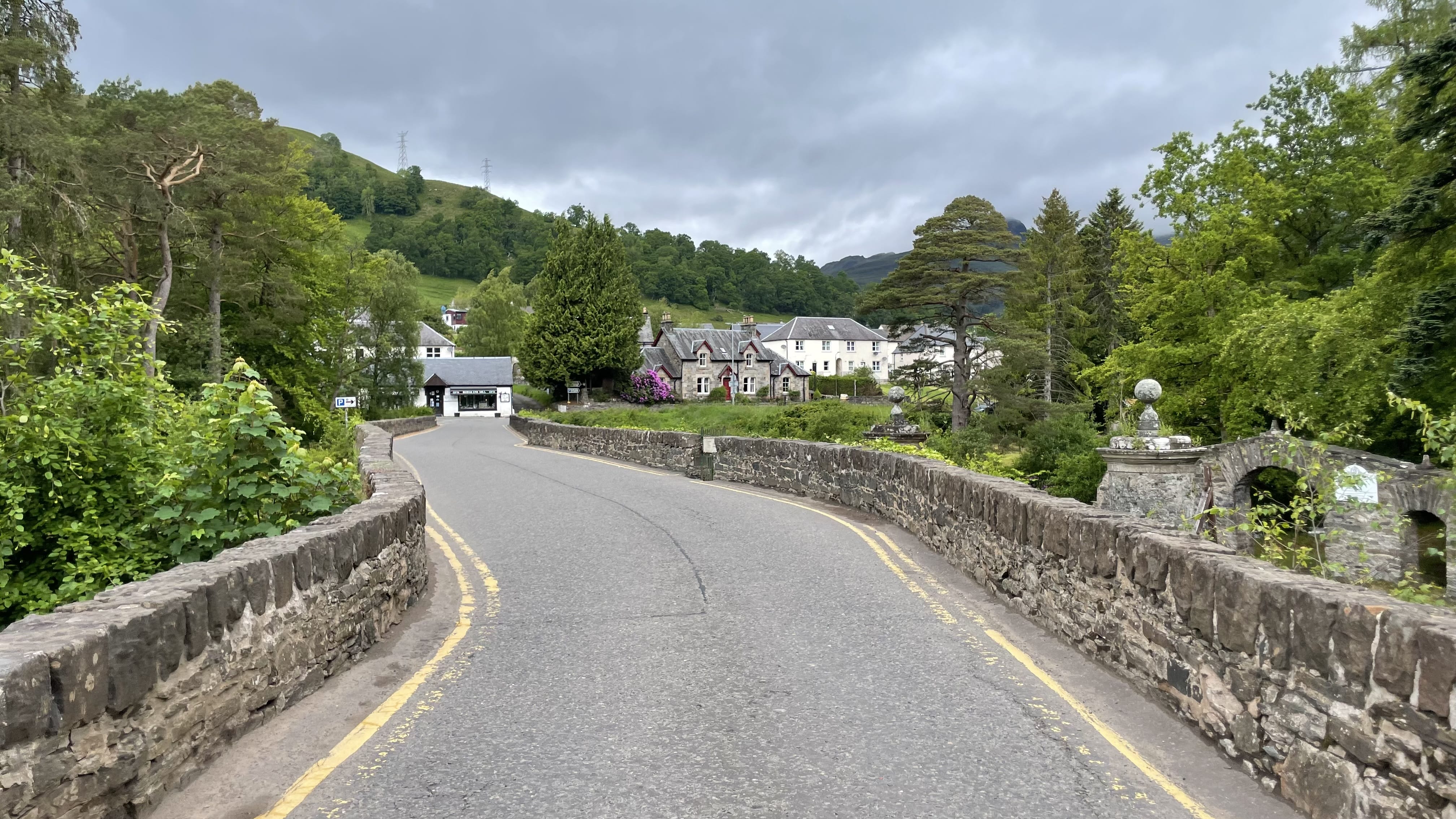 Stone bridge at the edge of Killin, Scotland, surrounded by lush greenery and cottages, marking the start of the trail.