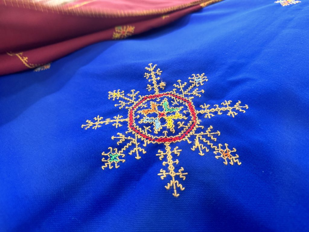 Close-up of traditional Berber embroidery on deep blue fabric, with colorful geometric patterns stitched in yellow, red, green, and blue.