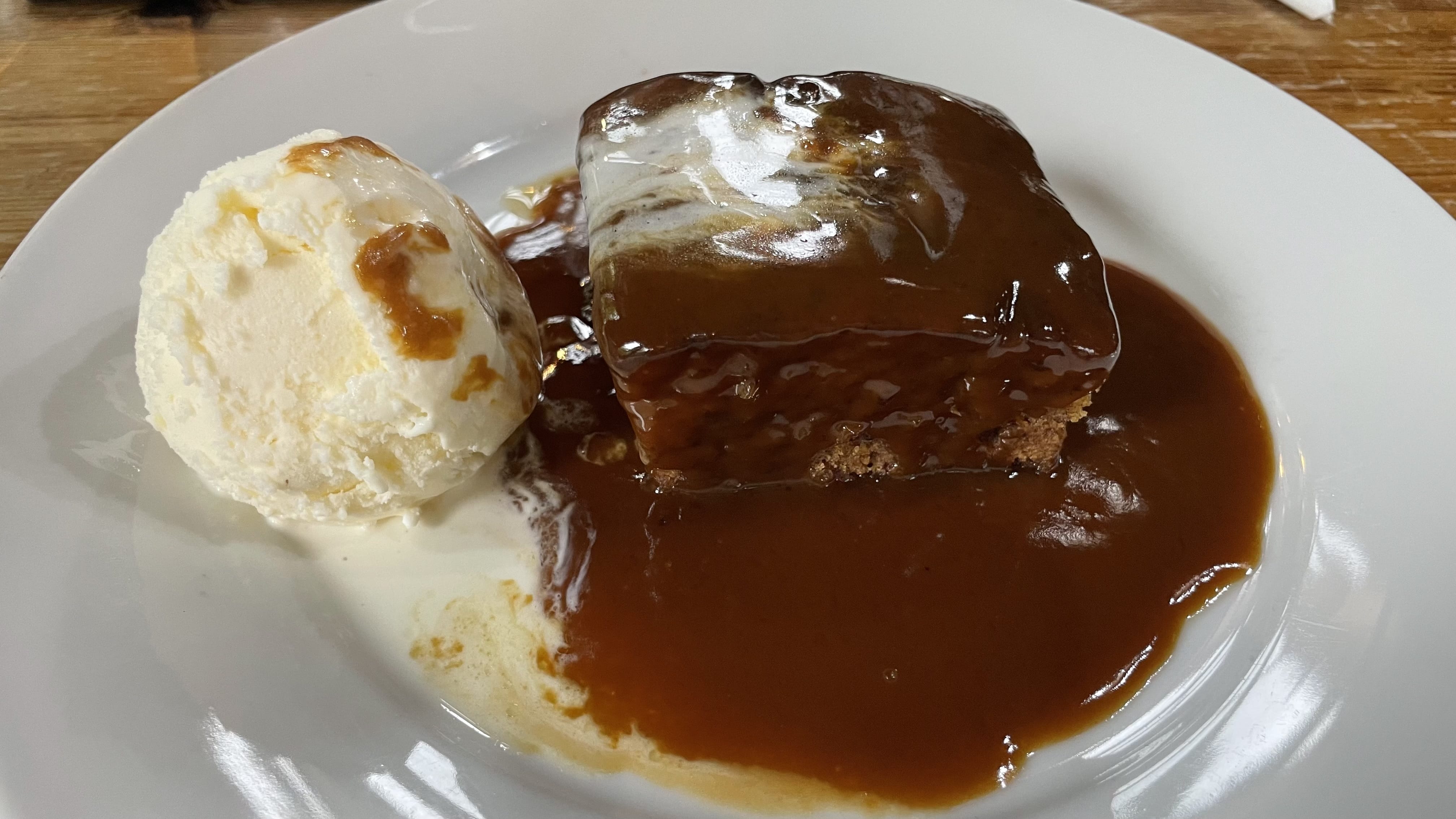 A plate of sticky toffee pudding drenched in caramel sauce, served with a scoop of vanilla ice cream.
