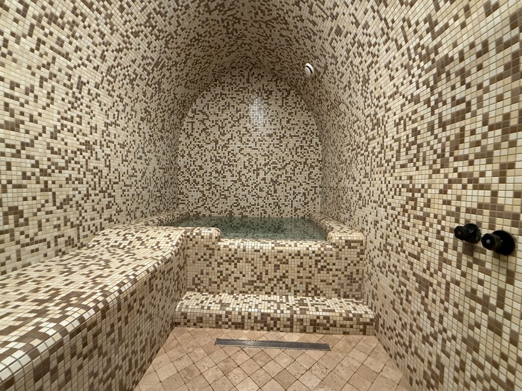 Small private sulfur pool lined with beige mosaic tiles inside a Tbilisi sulfur bath.