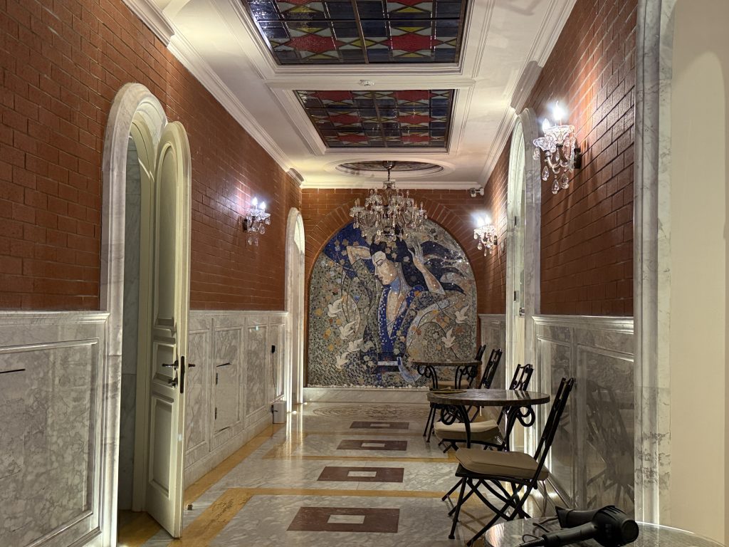 Luxurious waiting area inside one of Tbilisi’s sulfur baths, featuring chandeliers, a mosaic mural, and marble walls.