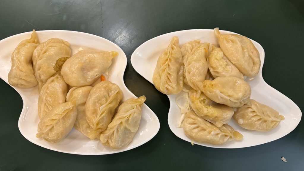 Plates of steamed Tibetan momos filled with vegetables, served on white curved dishes.