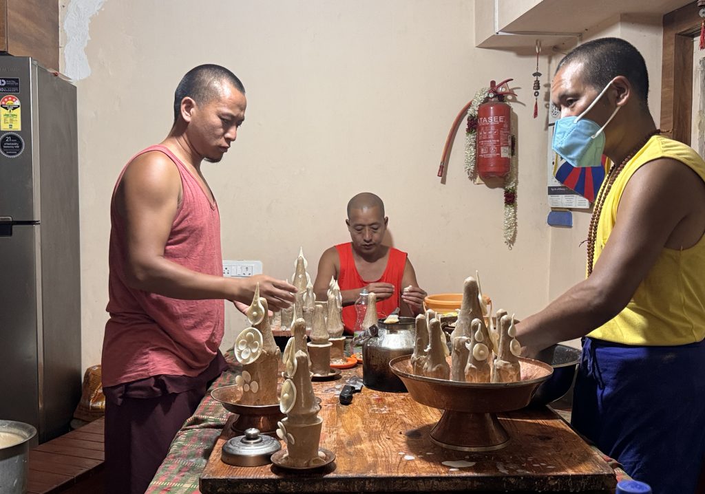 Monks in sleeveless shirts sculpting traditional butter offerings by hand at a work table.