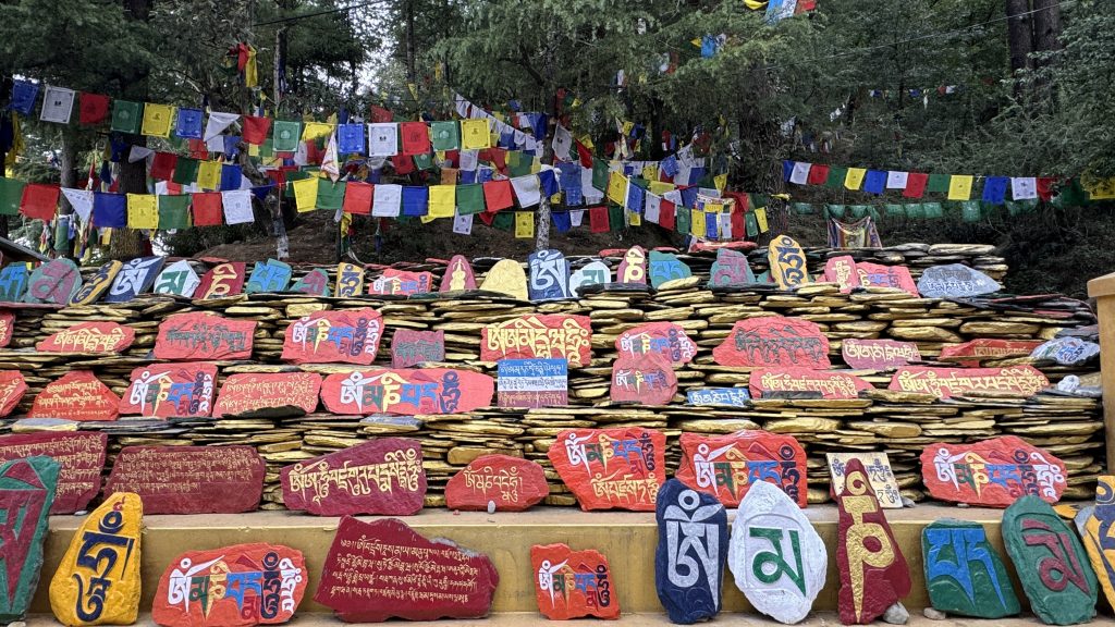 Painted mani stones inscribed with Tibetan mantras stacked beneath rows of prayer flags.
