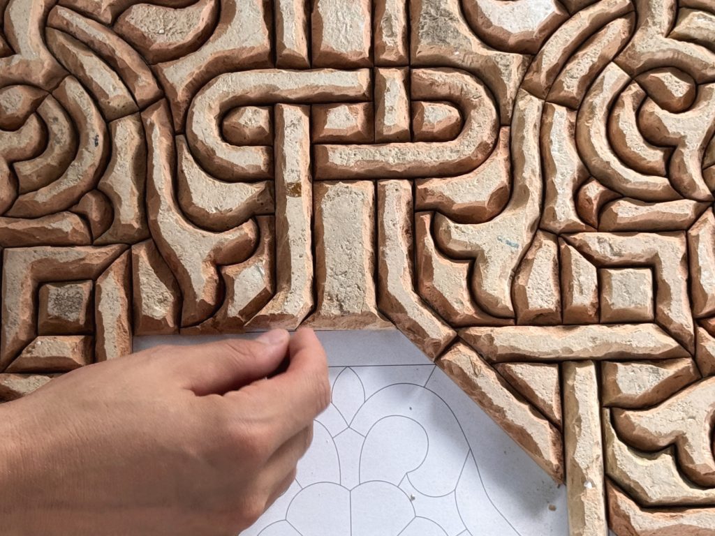 Close-up of an artisan’s hand placing terracotta zellige tiles in an intricate pattern during a workshop visit on 2 Days in Fes.