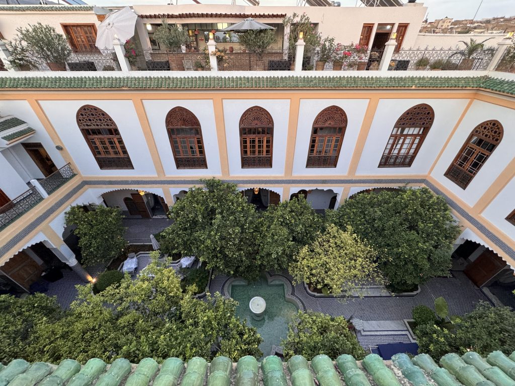 View from above of the central courtyard atEden at Palais Amani, with a small fountain, citrus trees, and arched balconies, during 2 Days in Fes.