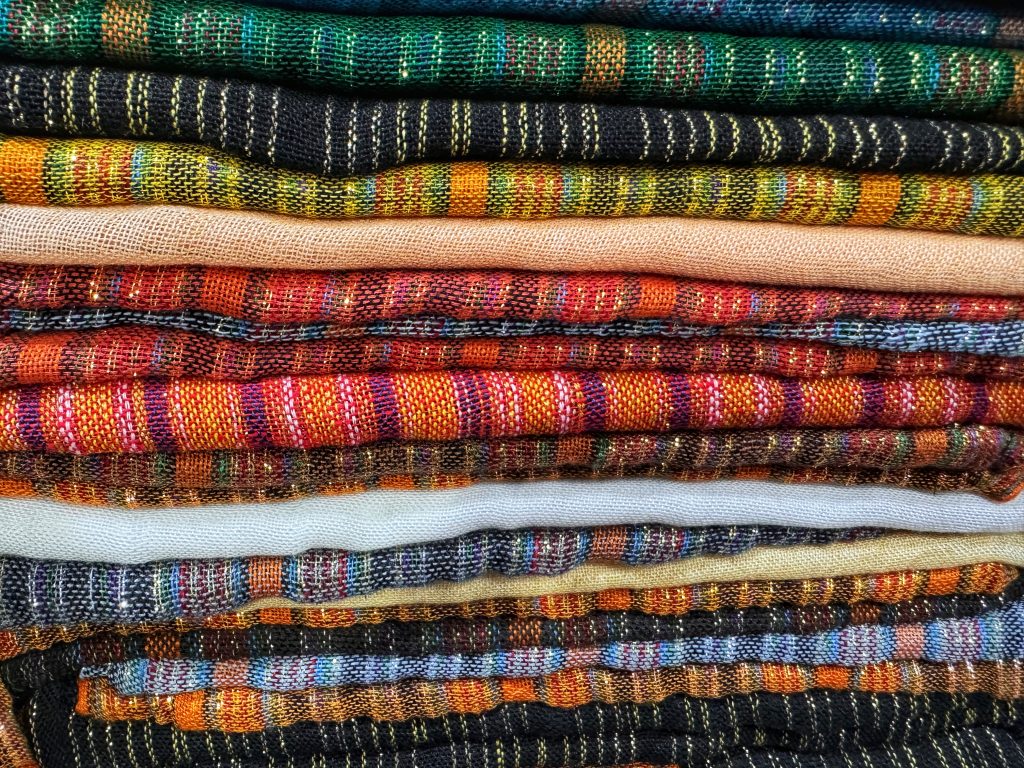 Stack of folded Moroccan handwoven scarves in bright, colorful patterns, seen during 2 Days in Fes.