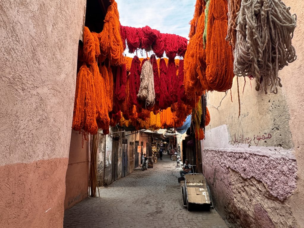 Bright bundles of orange, red, and beige wool hang overhead in a narrow Marrakech alley—two days in marrakech