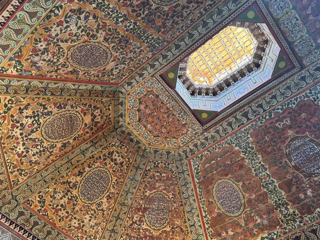 Ornate painted wooden ceiling panels with floral motifs and a skylight at Bahia Palace.