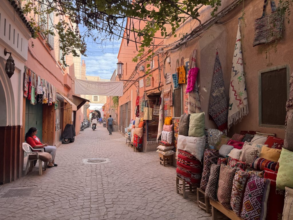 Colorful rugs, pillows, and bags displayed along a narrow alley in the Marrakech medina – 2 days in Marrakech.