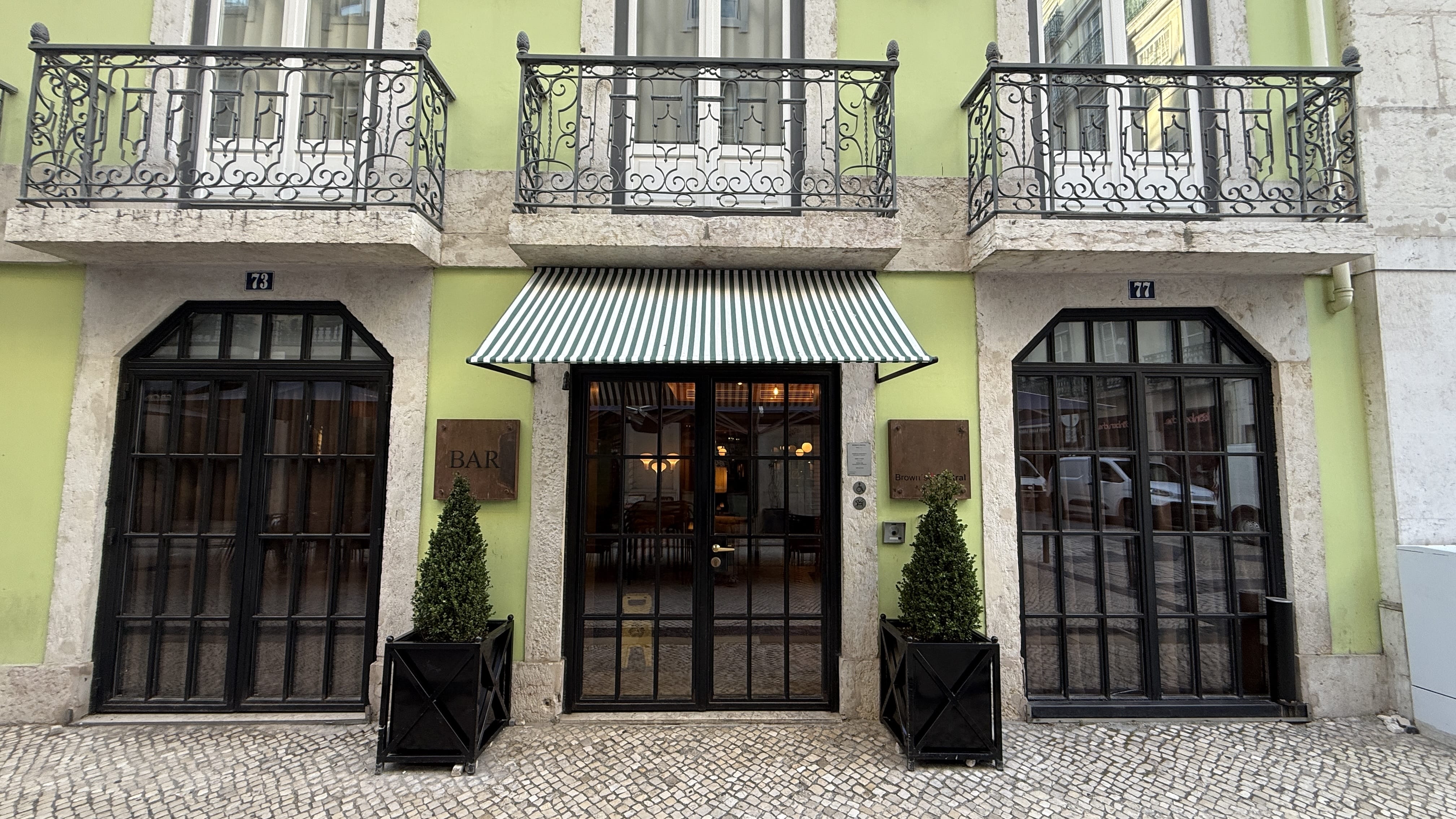 Entrance to Brown’s Central Hotel in Lisbon with green-painted façade, black-framed windows, striped awning, and wrought iron balconies.
