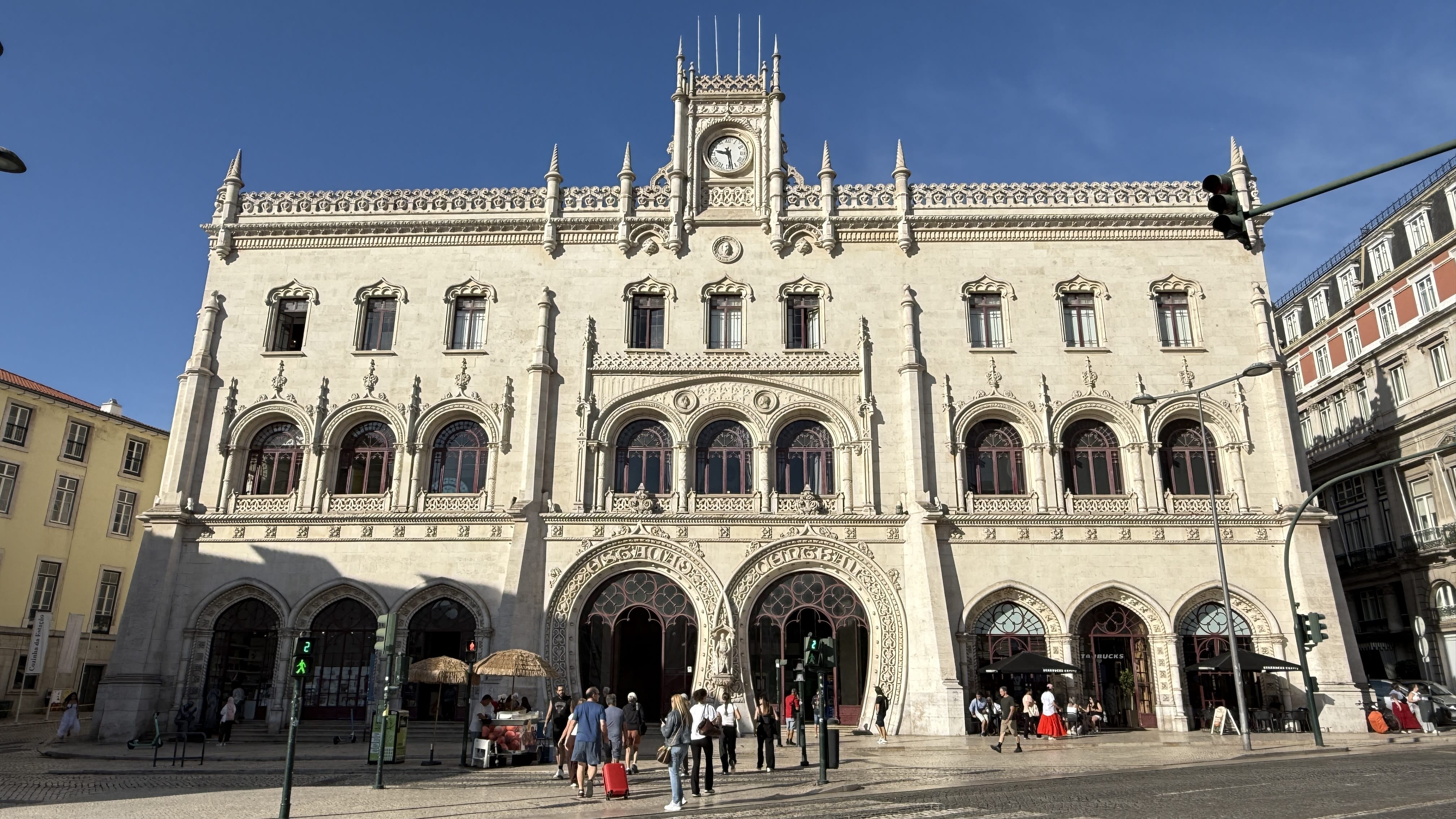Neo-Manueline facade of Rossio Train Station in Lisbon with ornate arches and clock tower.