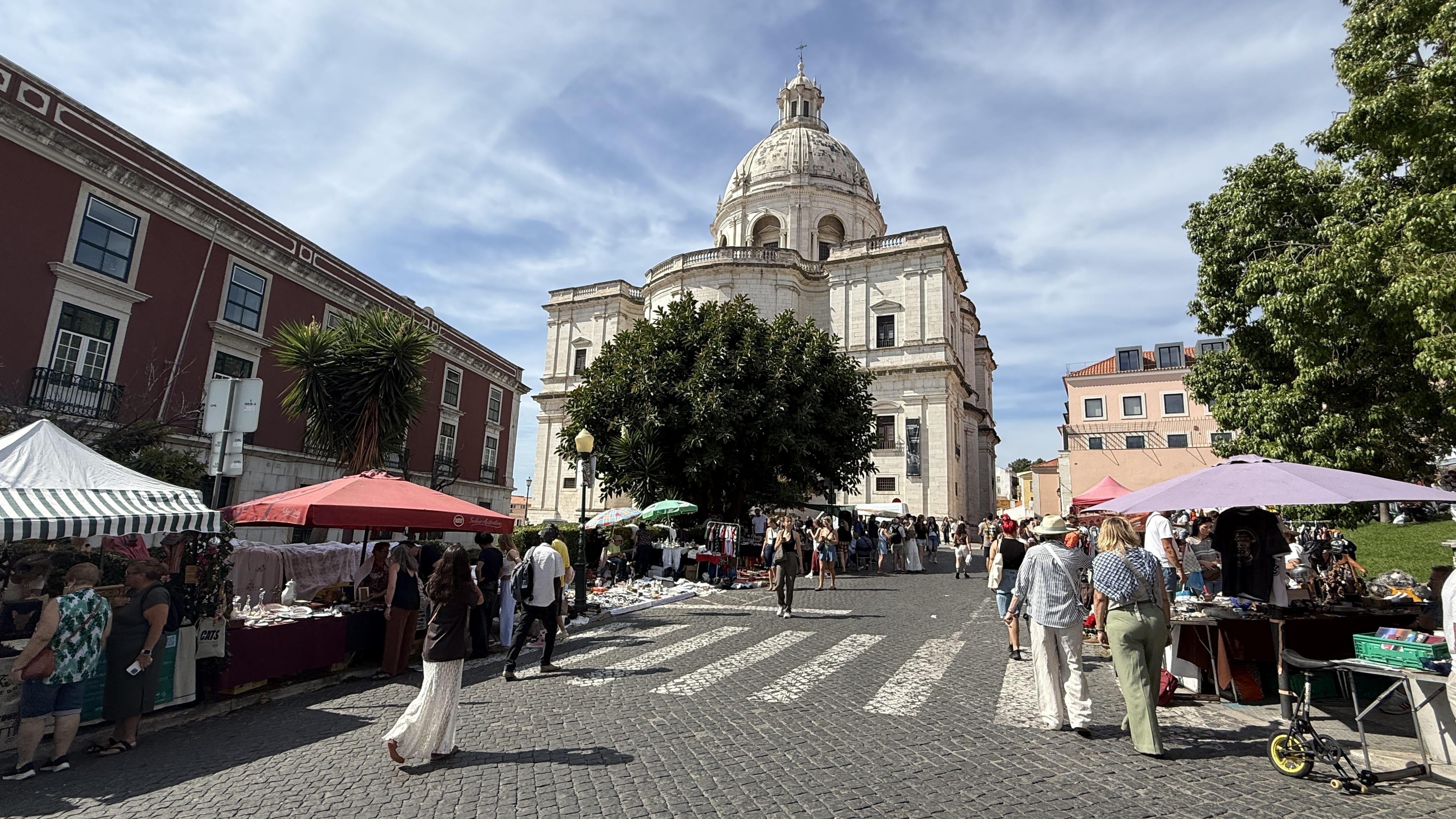 Feira da Ladra flea market in front of the National Pantheon in Lisbon, with stalls, vendors, and crowds on a sunny day.