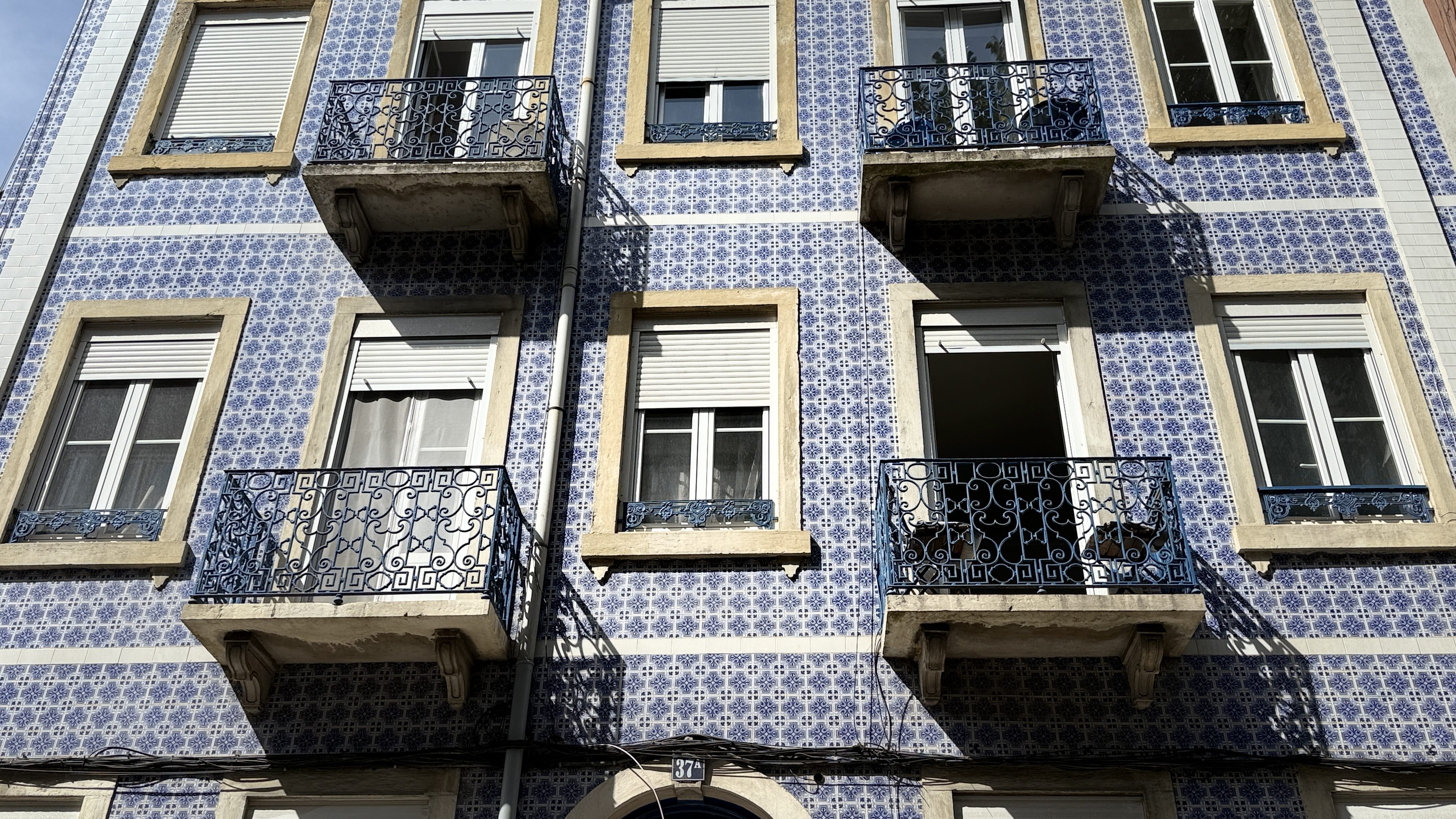 Lisbon building covered in bright blue azulejos with black wrought-iron balconies and plants.
