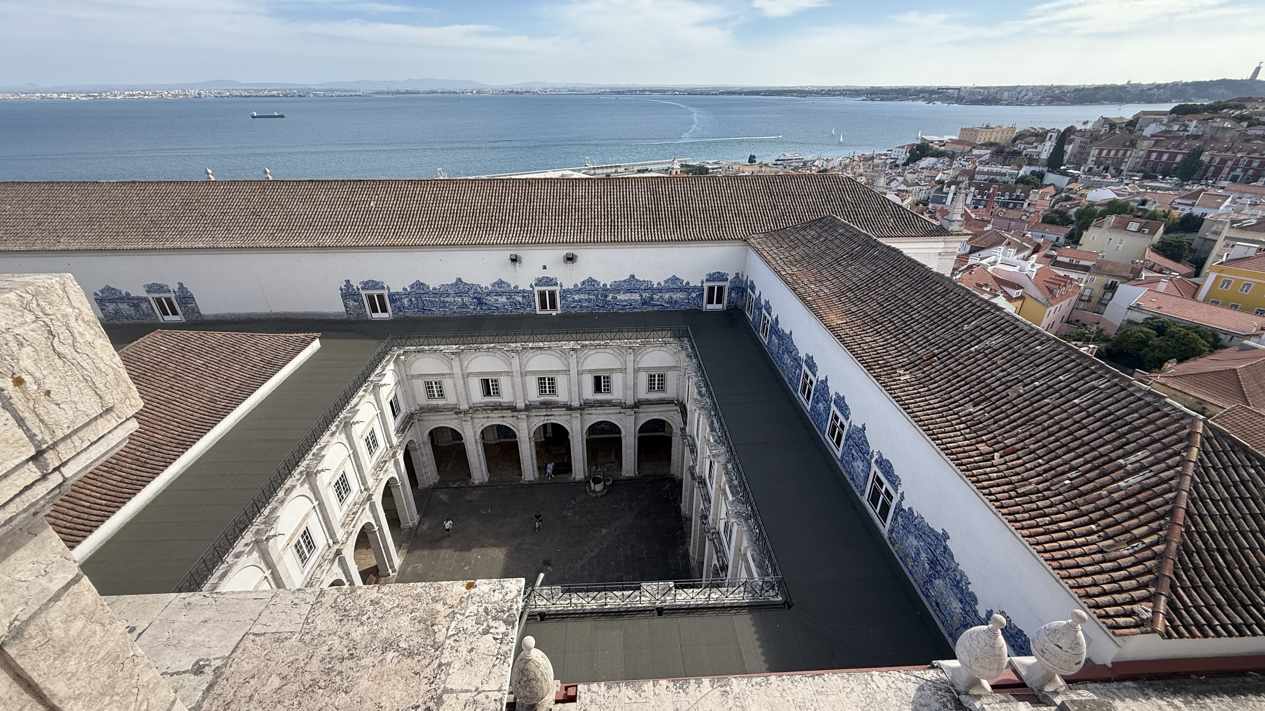 Aerial view of the cloister courtyard of São Vicente de Fora, lined with azulejo tiles, with the Tagus River in the background.