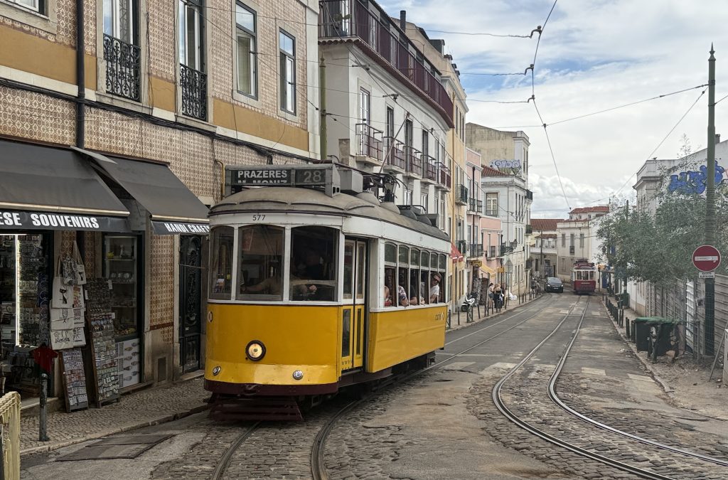 Historic yellow tram passing through the streets of Baixa, Lisbon, Portugal, with tiled sidewalks and old buildings in the background – 5 days in Lisbon travel blog.