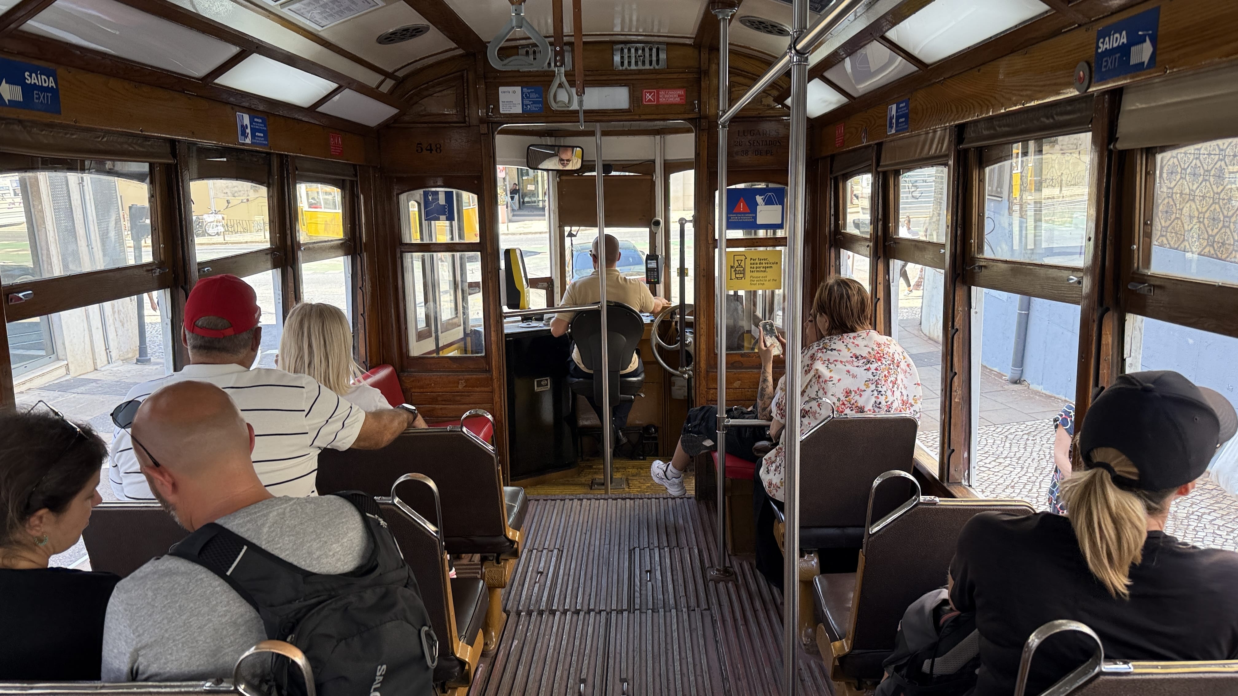 Interior of Lisbon’s historic Tram 28, with wooden seats, passengers, and views out to the city streets.