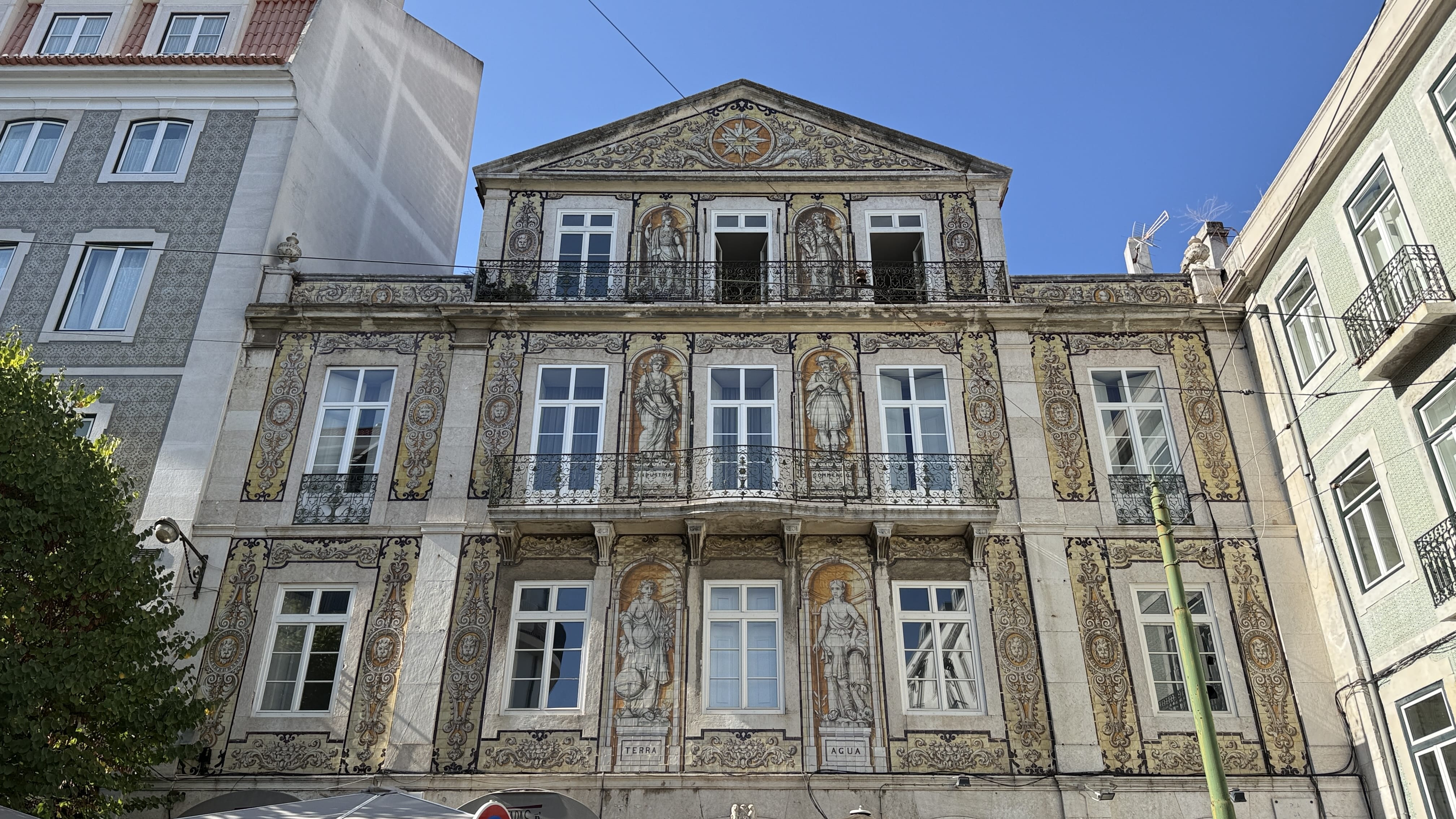 Ornate tiled façade of Casa do Ferreira das Tabuletas in Lisbon, Portugal, featuring neoclassical figures representing the four elements framed in azulejos under a bright blue sky.