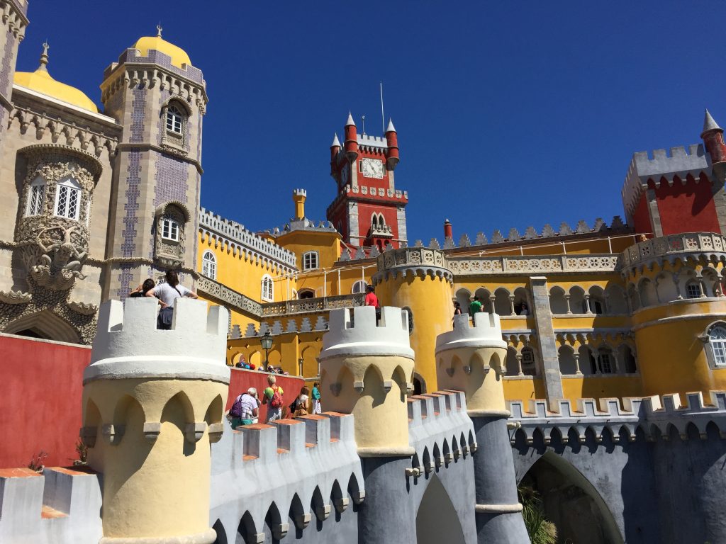 Bright yellow and red towers of Pena Palace in Sintra, Portugal, with visitors walking along the castle’s battlements.