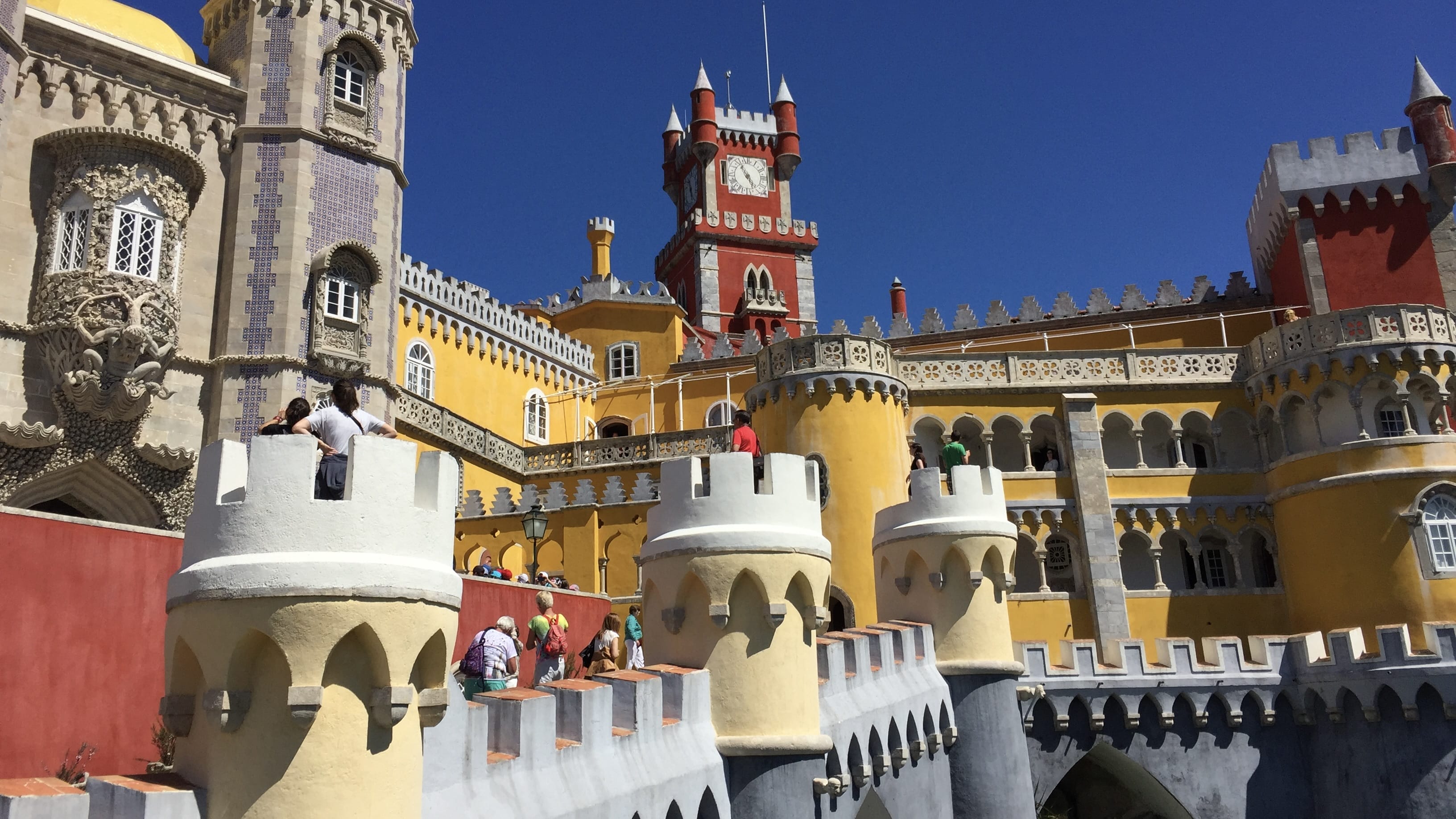Bright yellow and red towers of Pena Palace in Sintra, Portugal, with visitors walking along the castle’s battlements.
